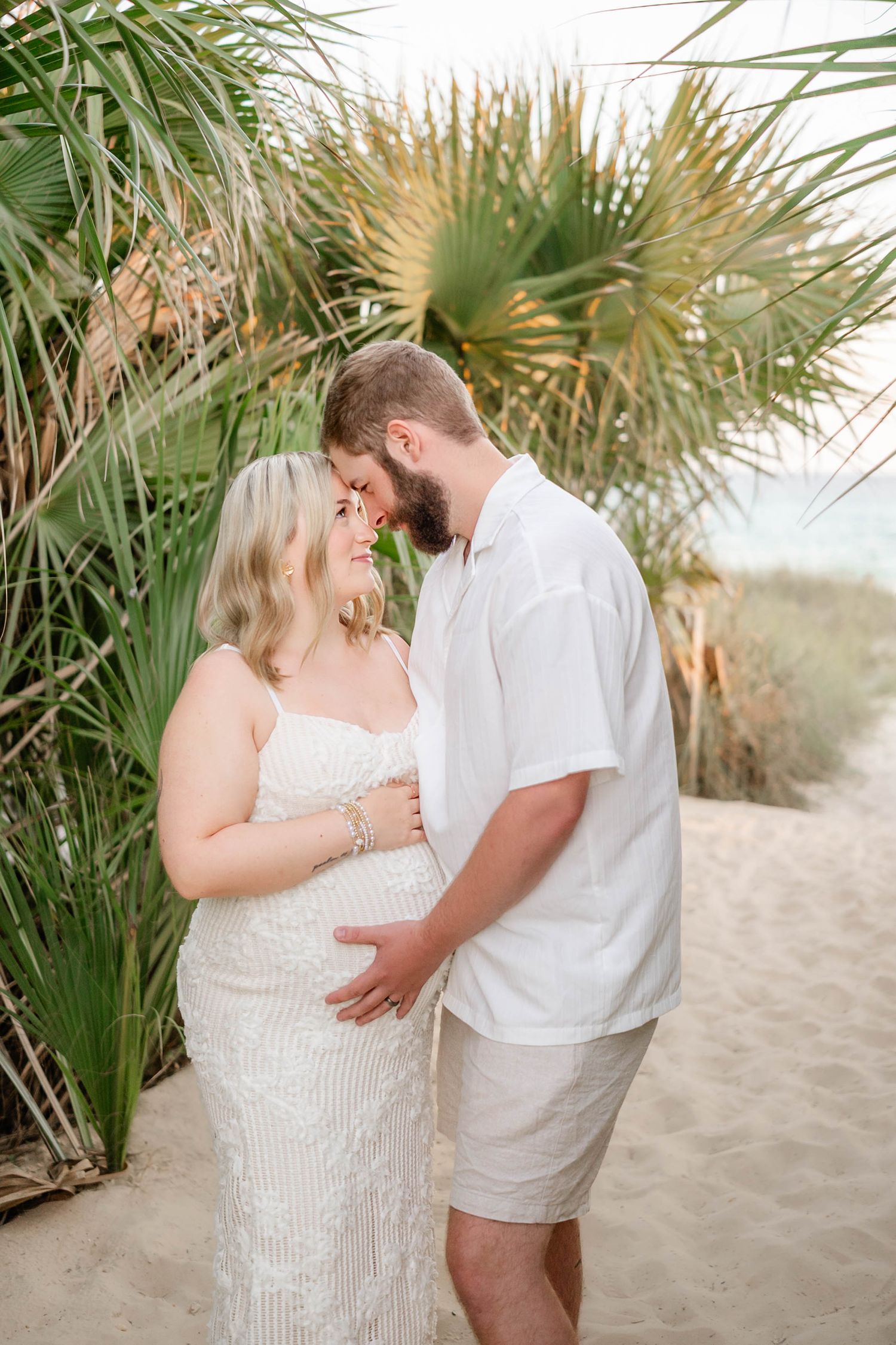 Maternity photoshoot among beach palm fronds with natural lighting.