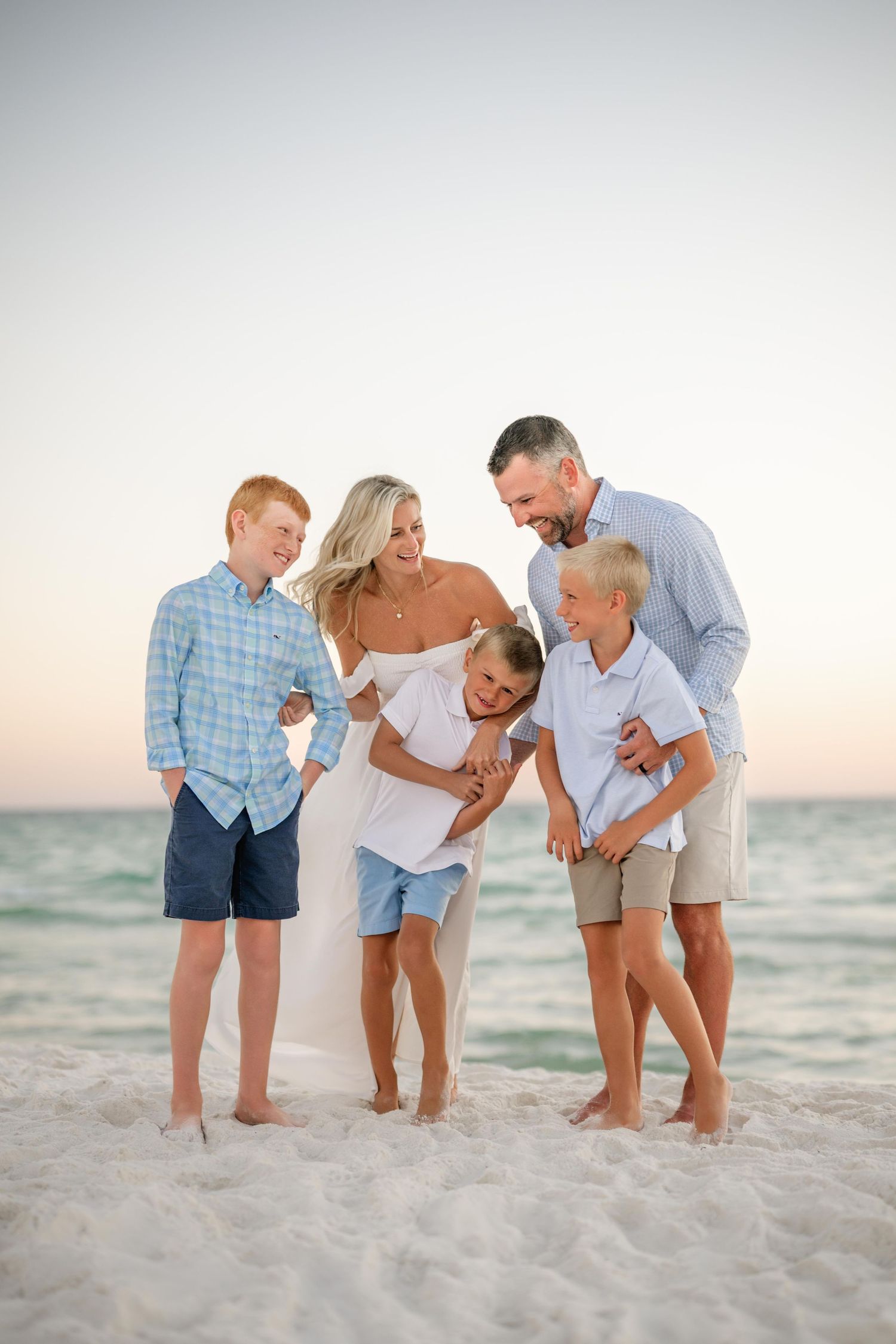 A family shares a candid laughing moment together on a white sandy beach at dusk.
