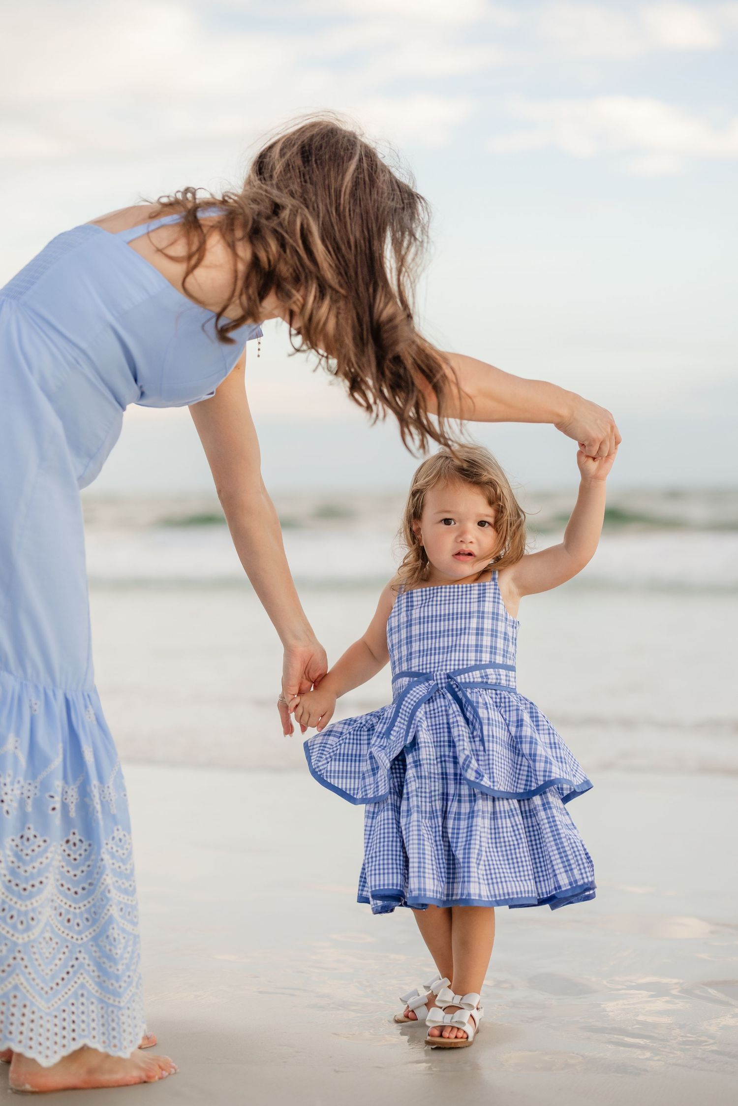 Close-up of matching blue dresses with eyelet details as mother and daughter play on the beach.