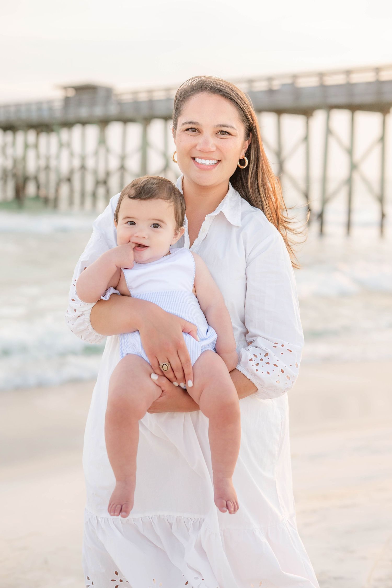 Mother and baby wearing white outfits during a beach photoshoot.