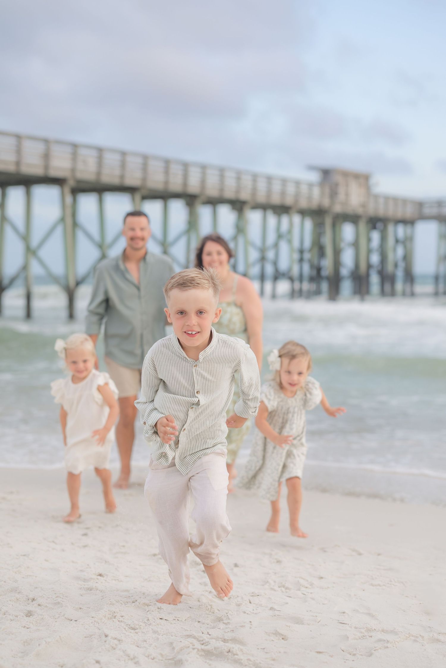Children running and playing on sandy beach with wooden pier in background.