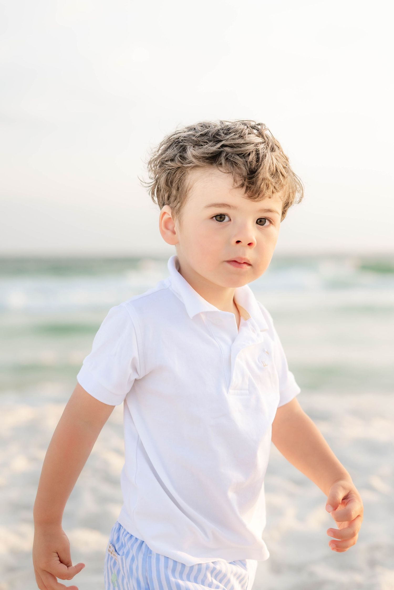 Child in white polo running along beach with ocean waves behind in Panama City Beach, Fl..