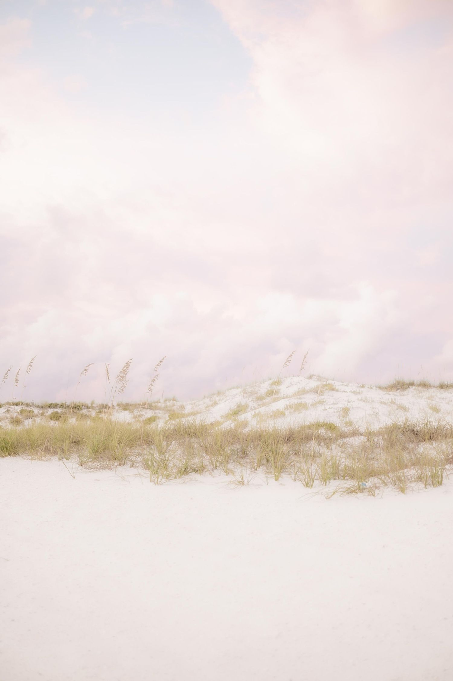 Pristine white sand dunes stretch across the horizon under a pastel pink sky.