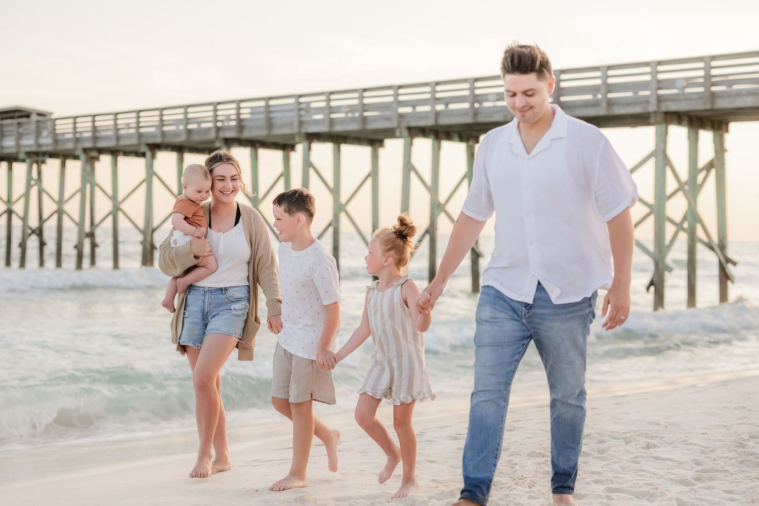 Group enjoying playful moments on beach with wooden pier structure visible in background.