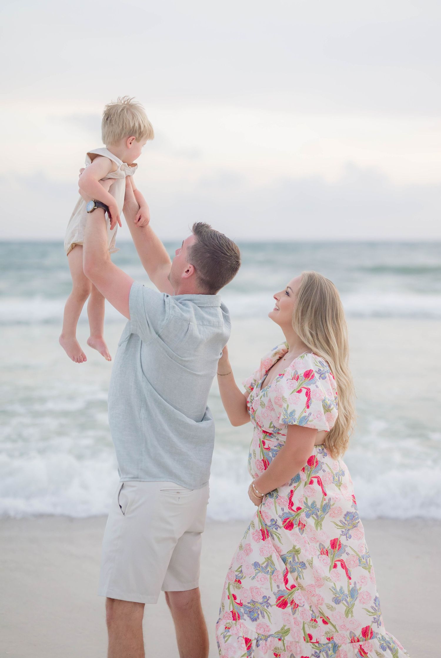 Parents play with their toddler on a misty beach during sunset.