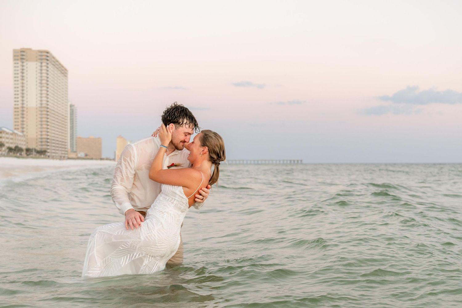 Romantic beach photography session with couple in water against coastal skyline.