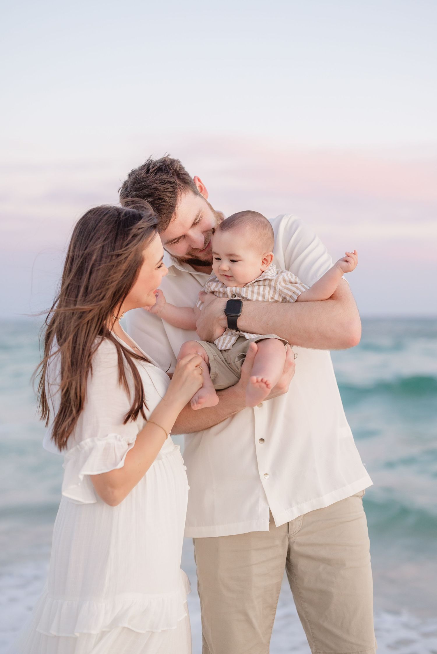 Family sharing tender moments together on a beach during sunset with the ocean waves in the background.