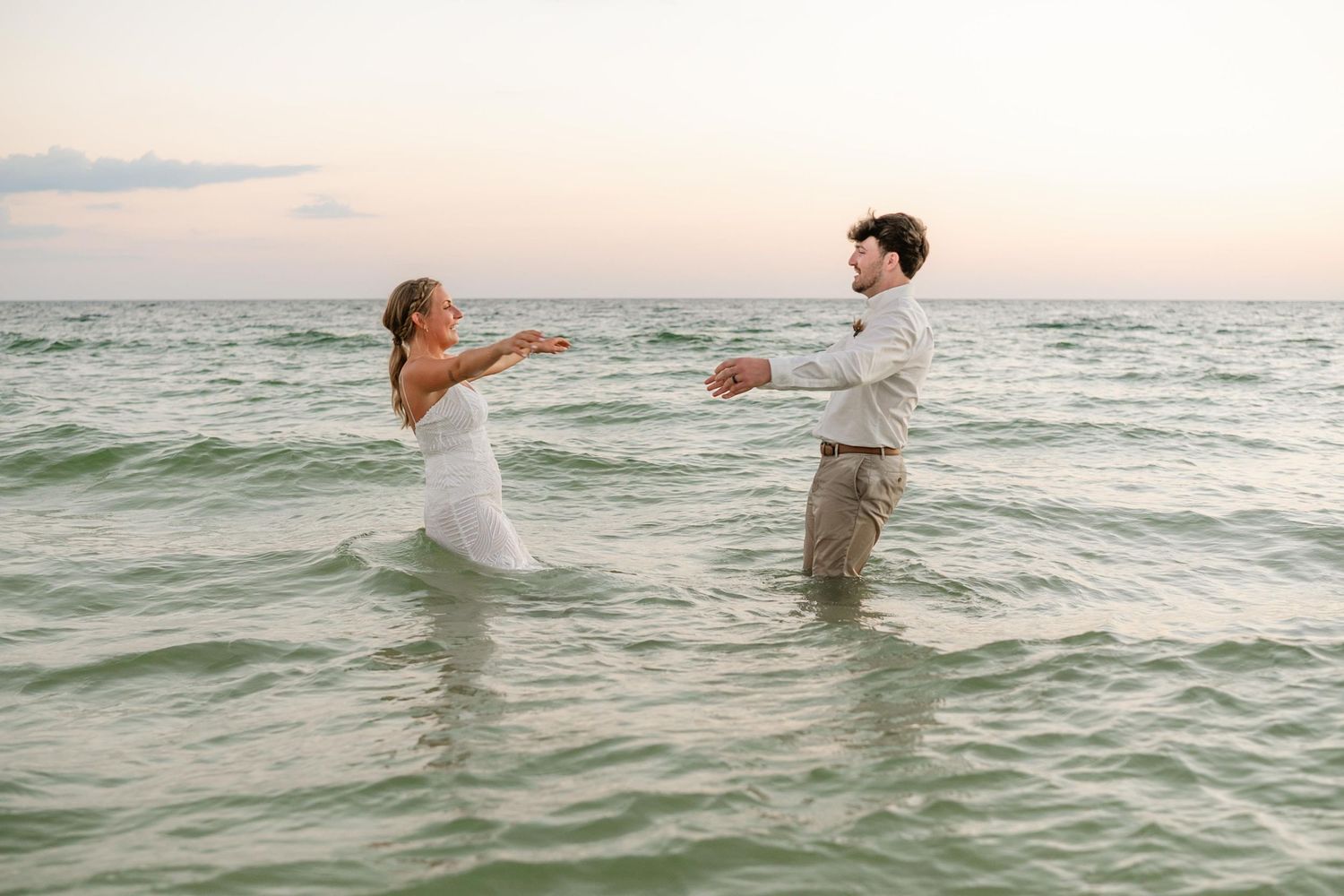 Playful couple splashes in ocean waves during sunset photo session.