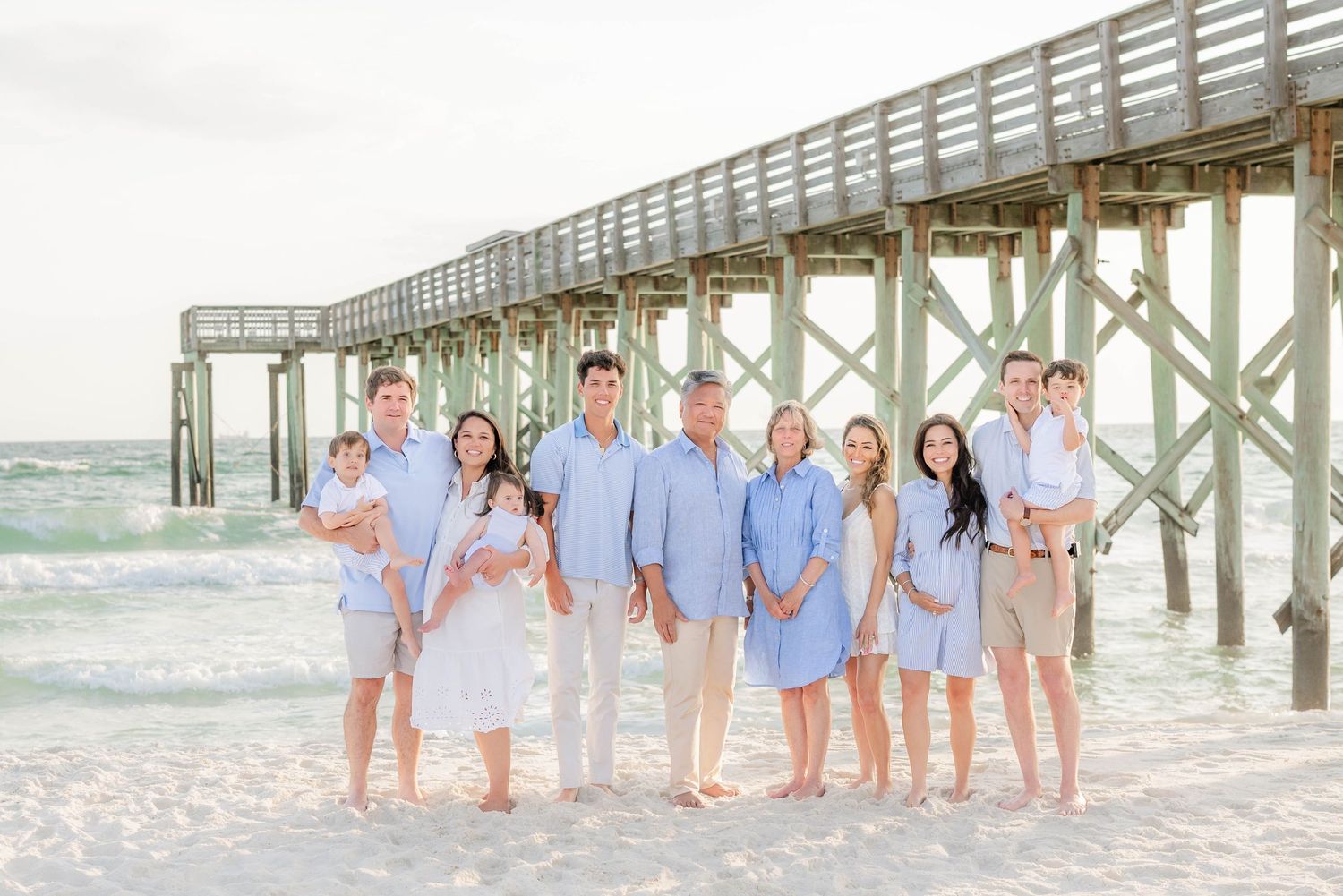 Family group wearing coordinated blue and white outfits posing by a wooden pier at the beach.