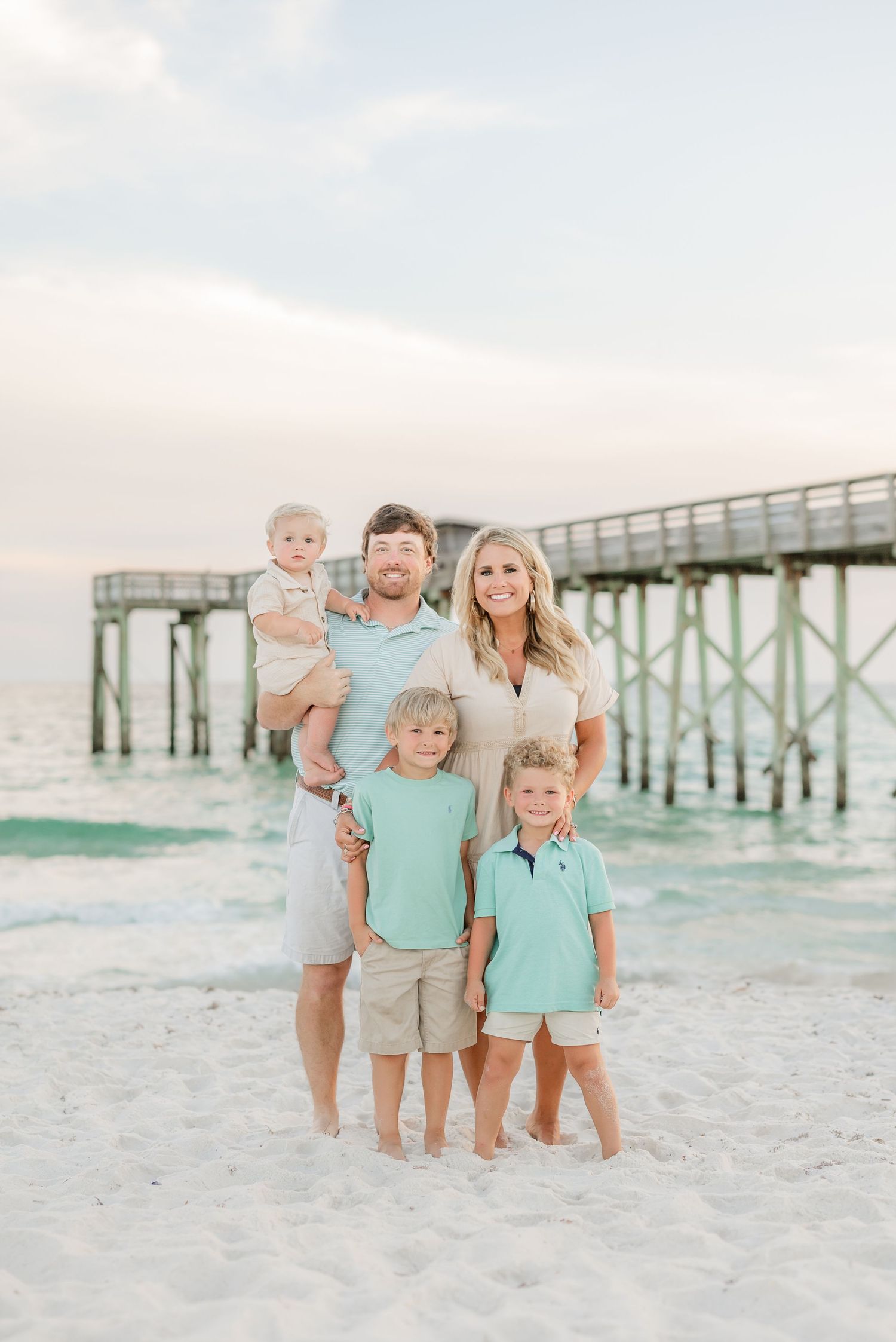 Family group wearing coordinated mint and neutral colors posing on white sand beach.