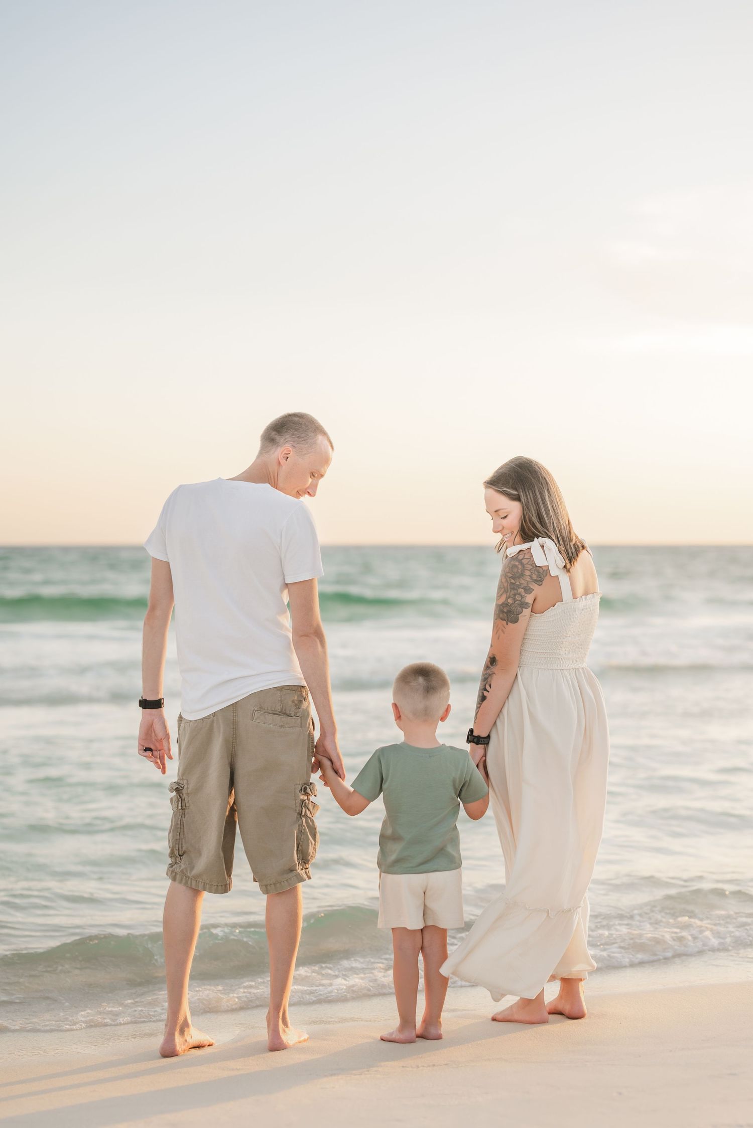A family holds hands while standing on a beach at sunset.