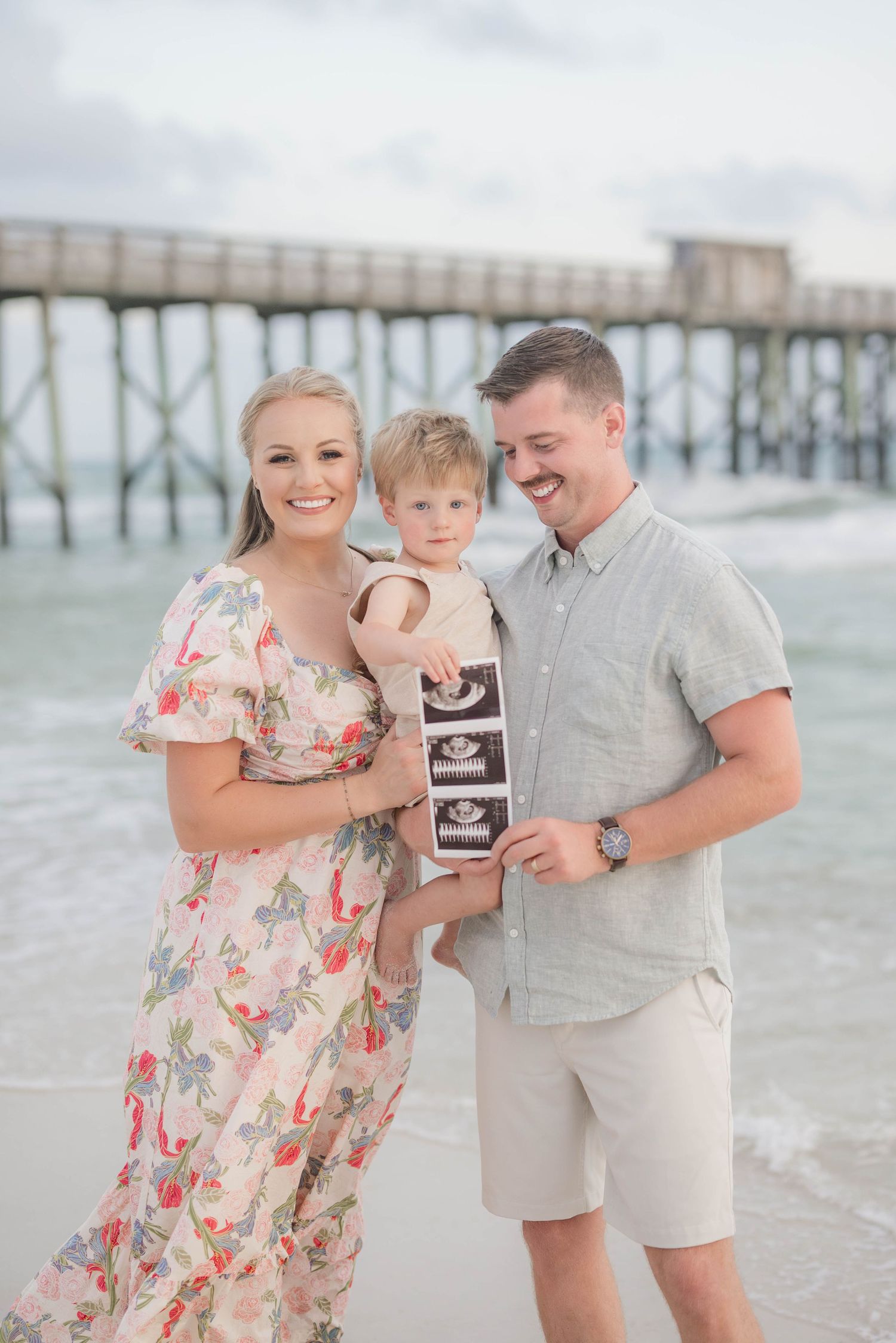 Family sharing special moment while holding ultrasound photo on beach.