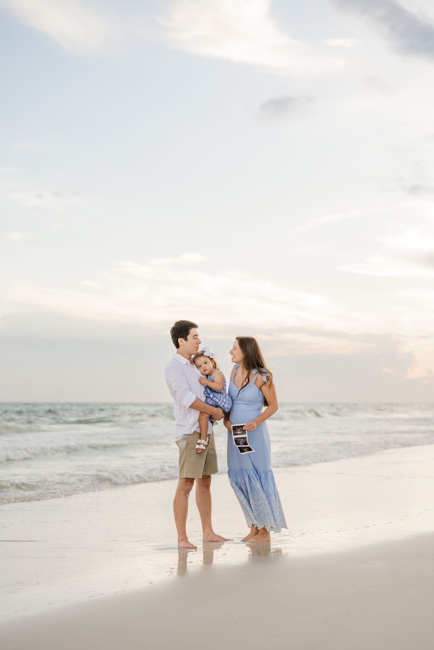 Family enjoying sunset moments together on white sandy beach by ocean waves.