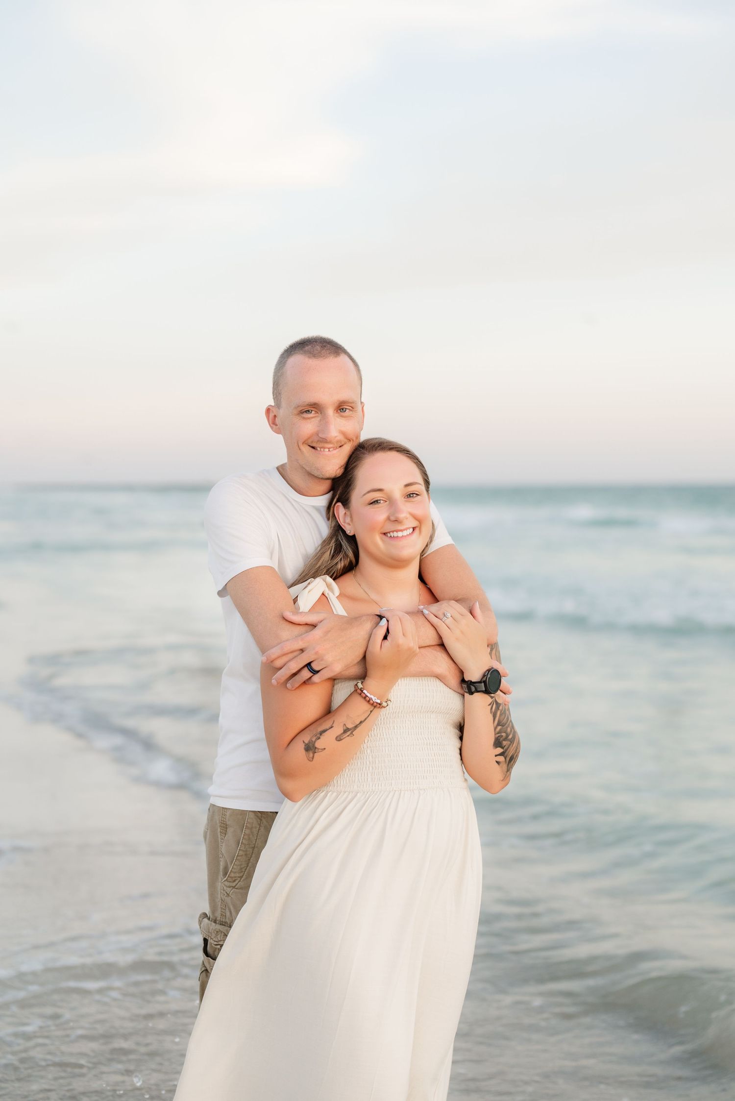 Sweet embrace captured during sunset beach photoshoot with ocean waves in background.
