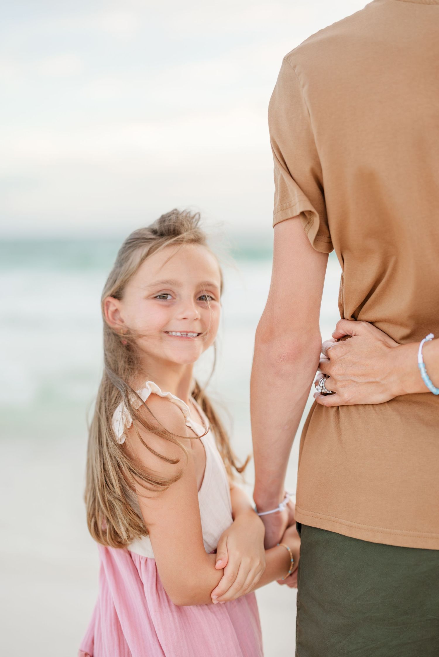 Mother and daughter hold hands while walking along the shoreline at sunset.