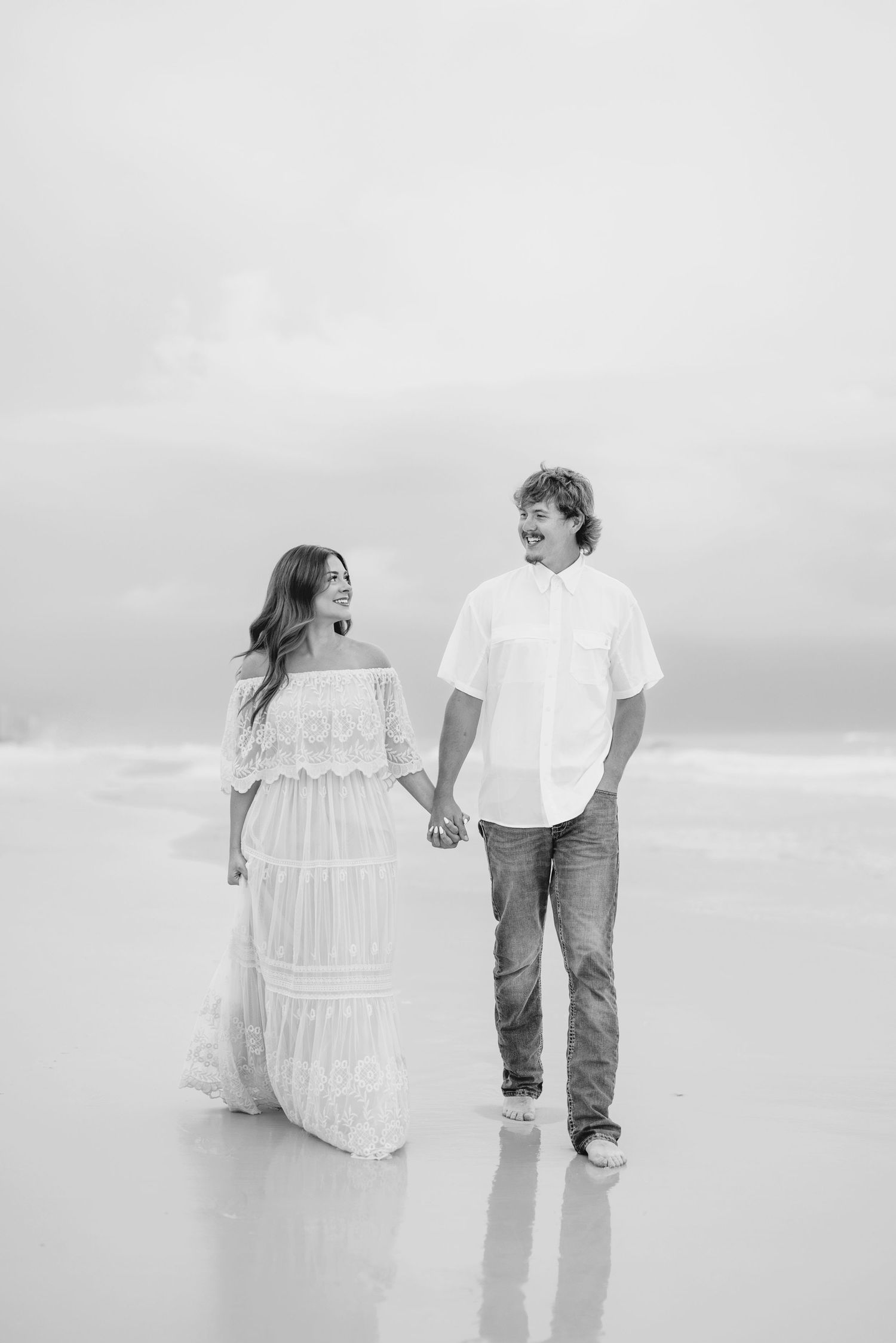 Black and white beach photography of couple sharing joyful moments by the ocean.