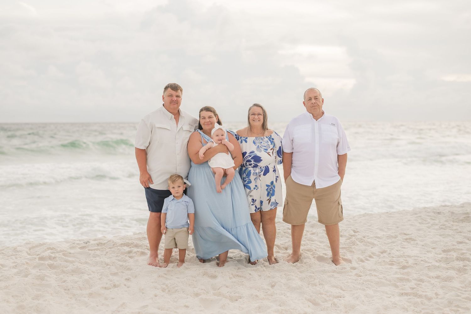 Family gathering on beach wearing coordinated blue and white outfits.