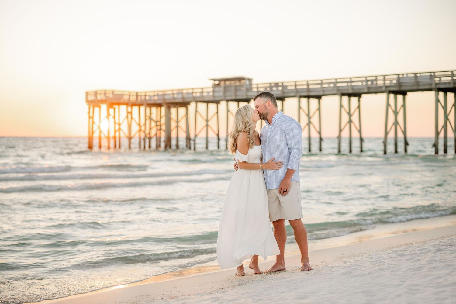 A romantic beach portrait with a wooden pier and golden sunset in the background.