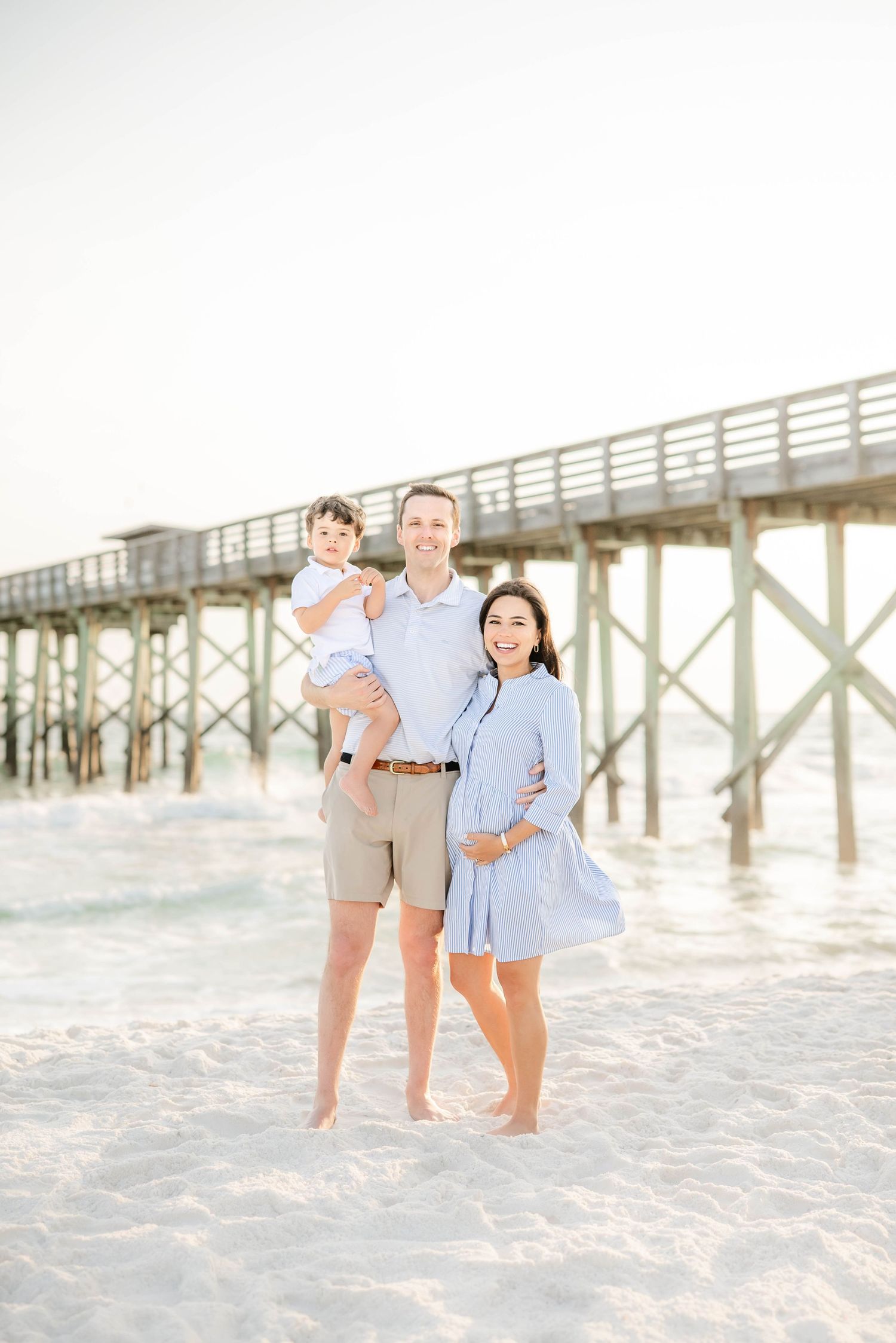 Casual family portrait session at the beach with a wooden pier in the background.