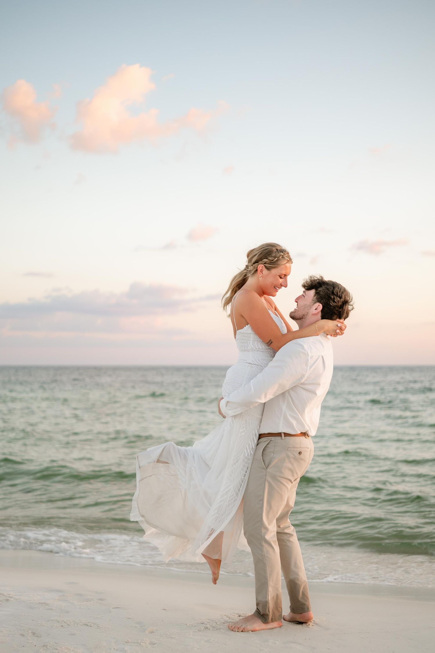 Beach wedding couple shares romantic moment on shoreline at sunset.