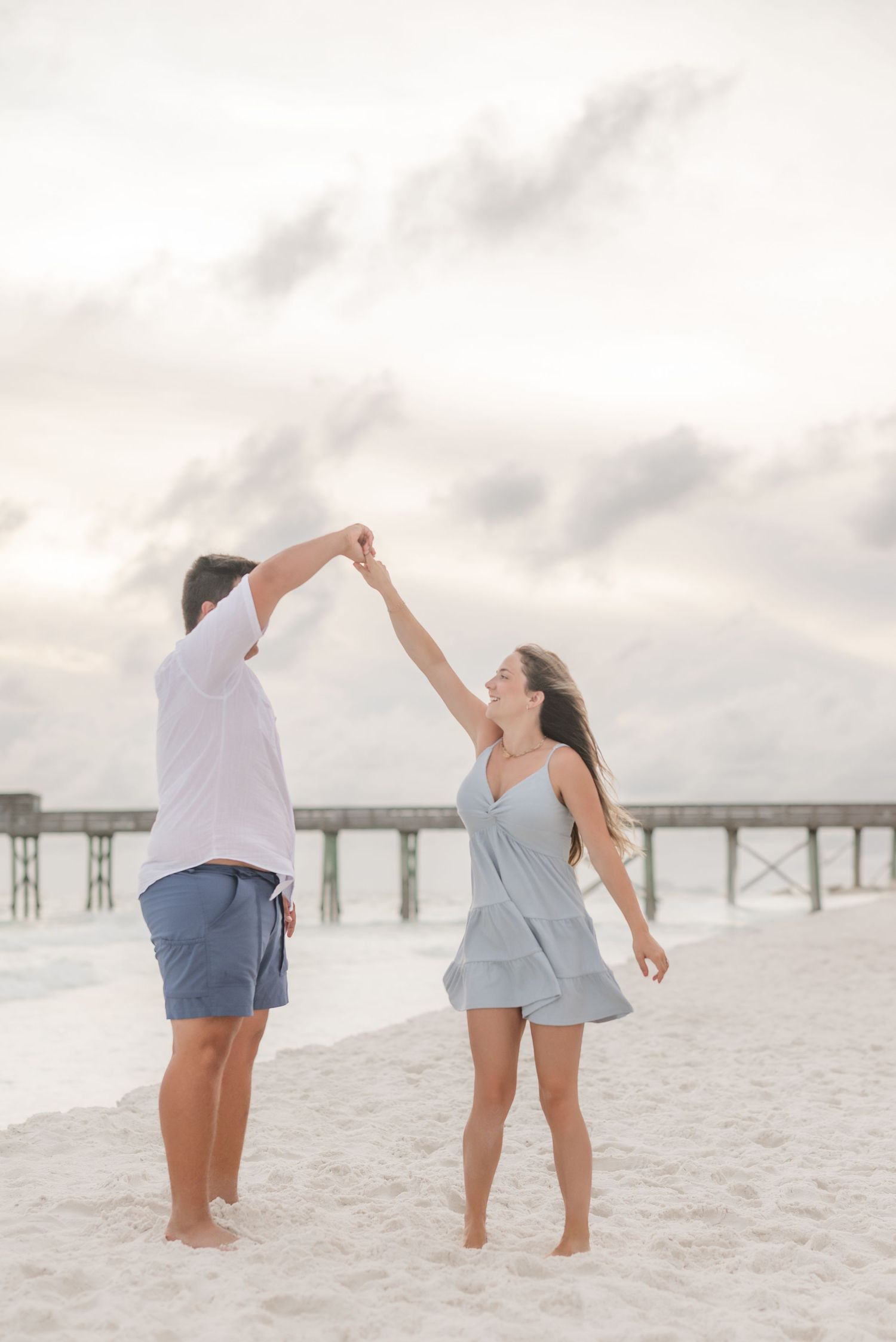 Couple dancing and twirling together on white sandy beach at dusk.