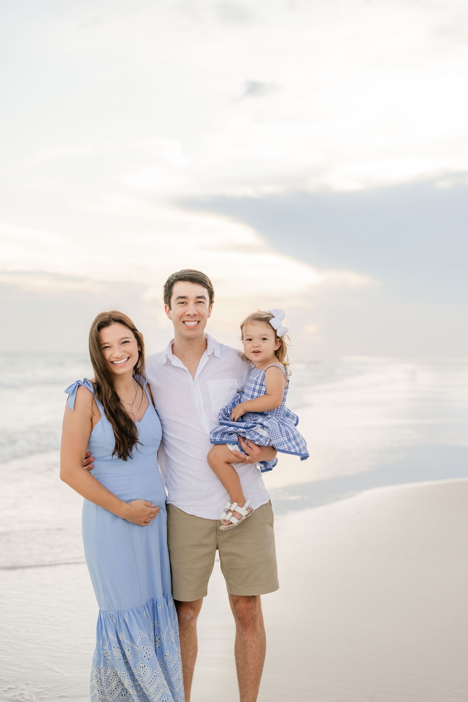 Family in coordinated blue and white outfits posing together on beach at sunset.