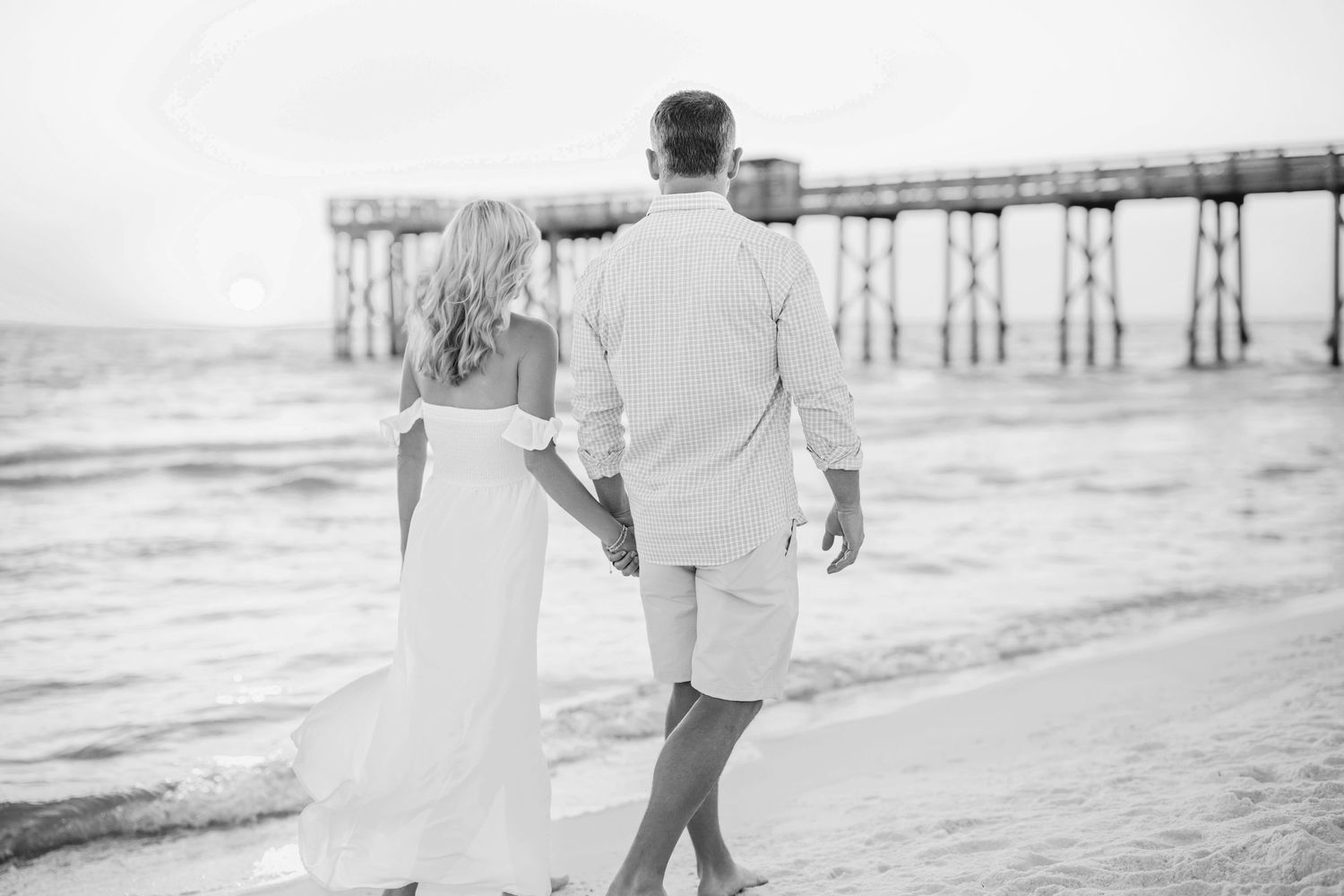 Couple walking together along a serene beach at sunset with soft waves in the background.