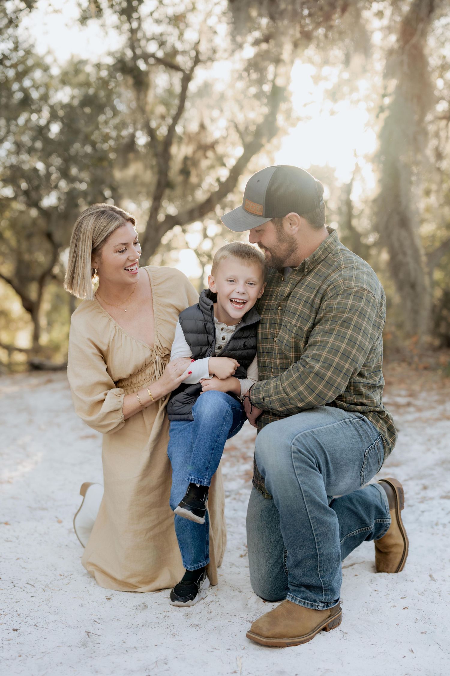 A family laughs together during an outdoor photo session in a wooded area.