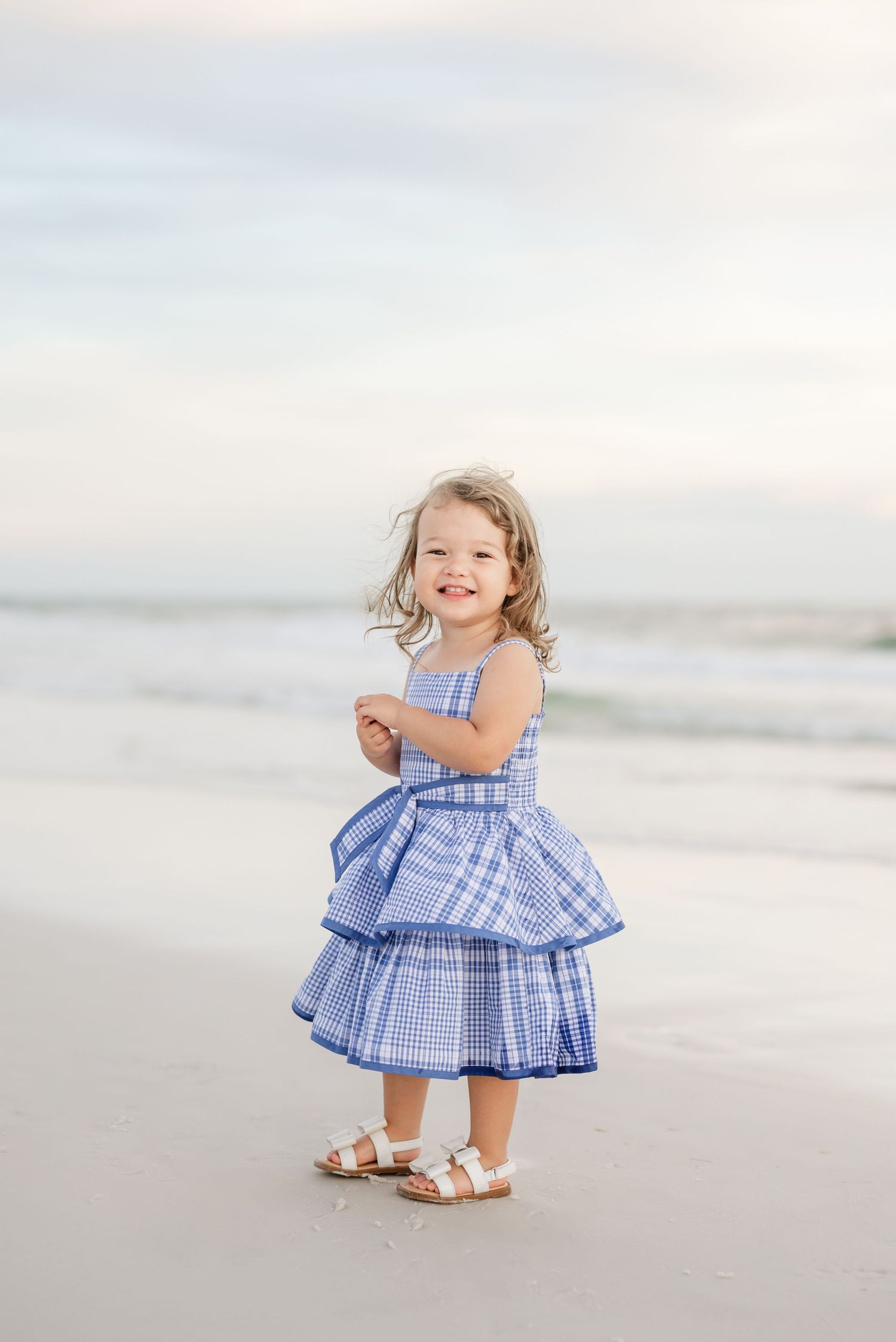 Child in blue checkered dress playing on beach during golden hour.