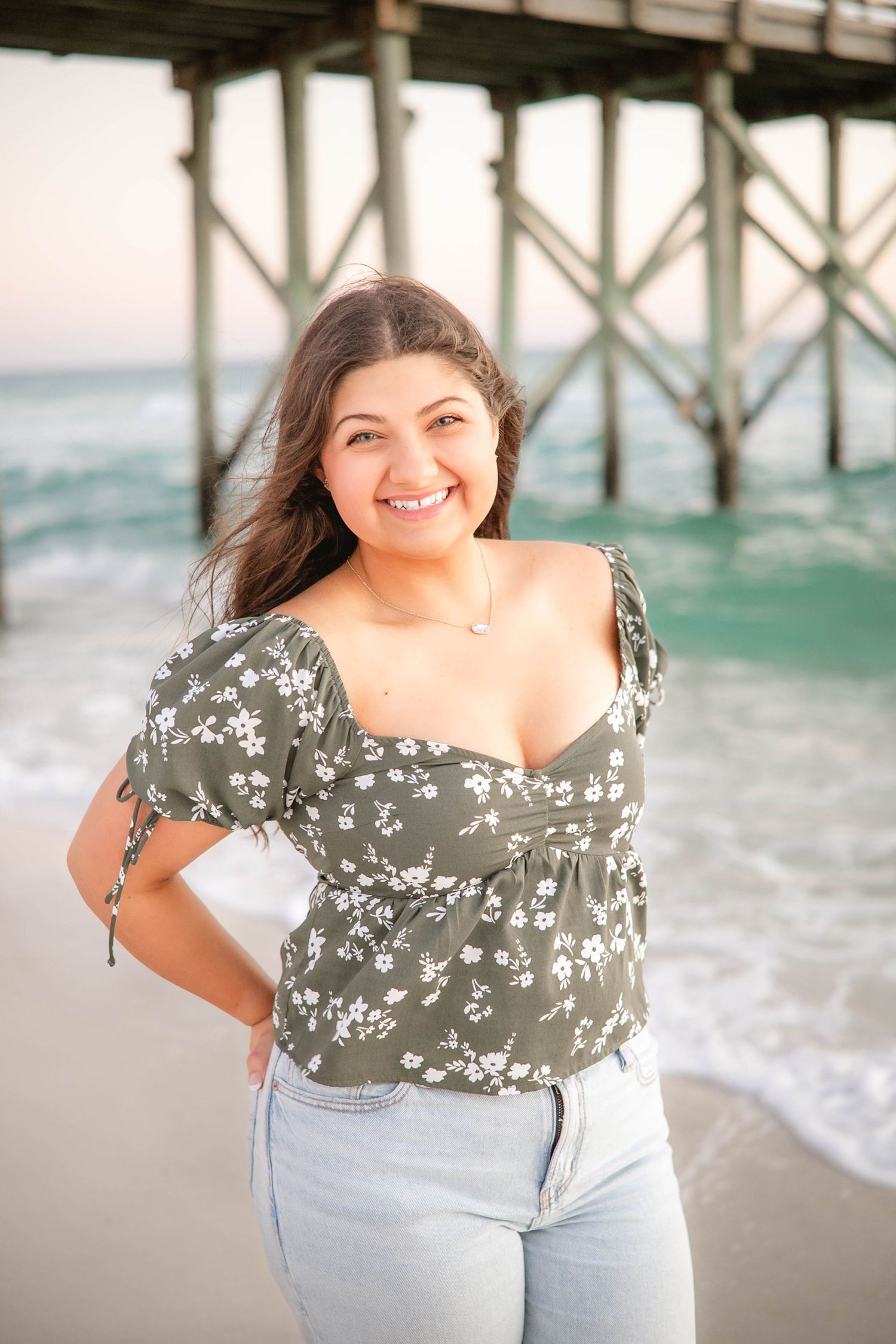 Casual beach photography under a wooden pier with waves crashing in the background.