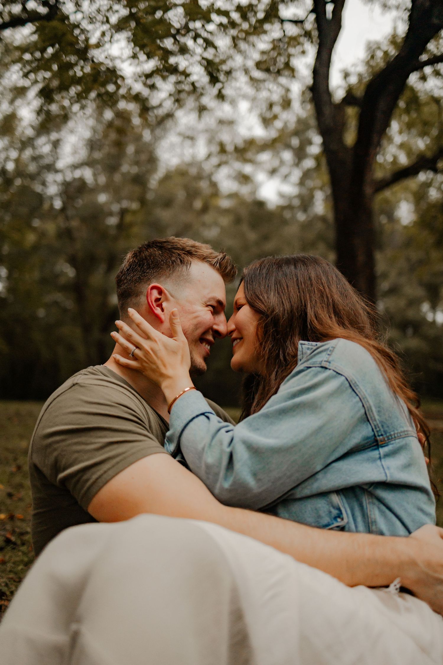 A couple sitting underneath a tree smiling and about to kiss
