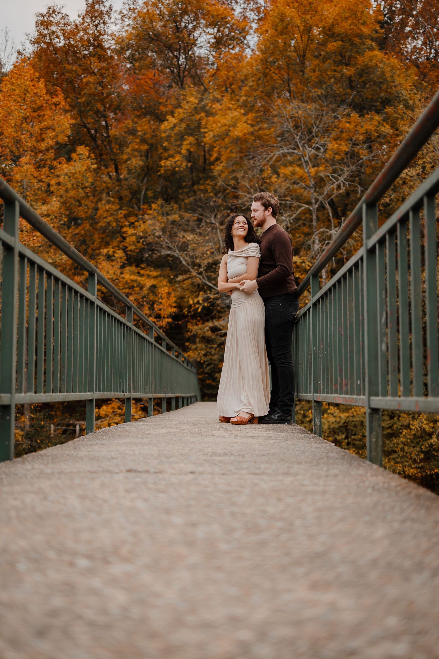 A couple dancing on a bridge with fall foliage behind them
