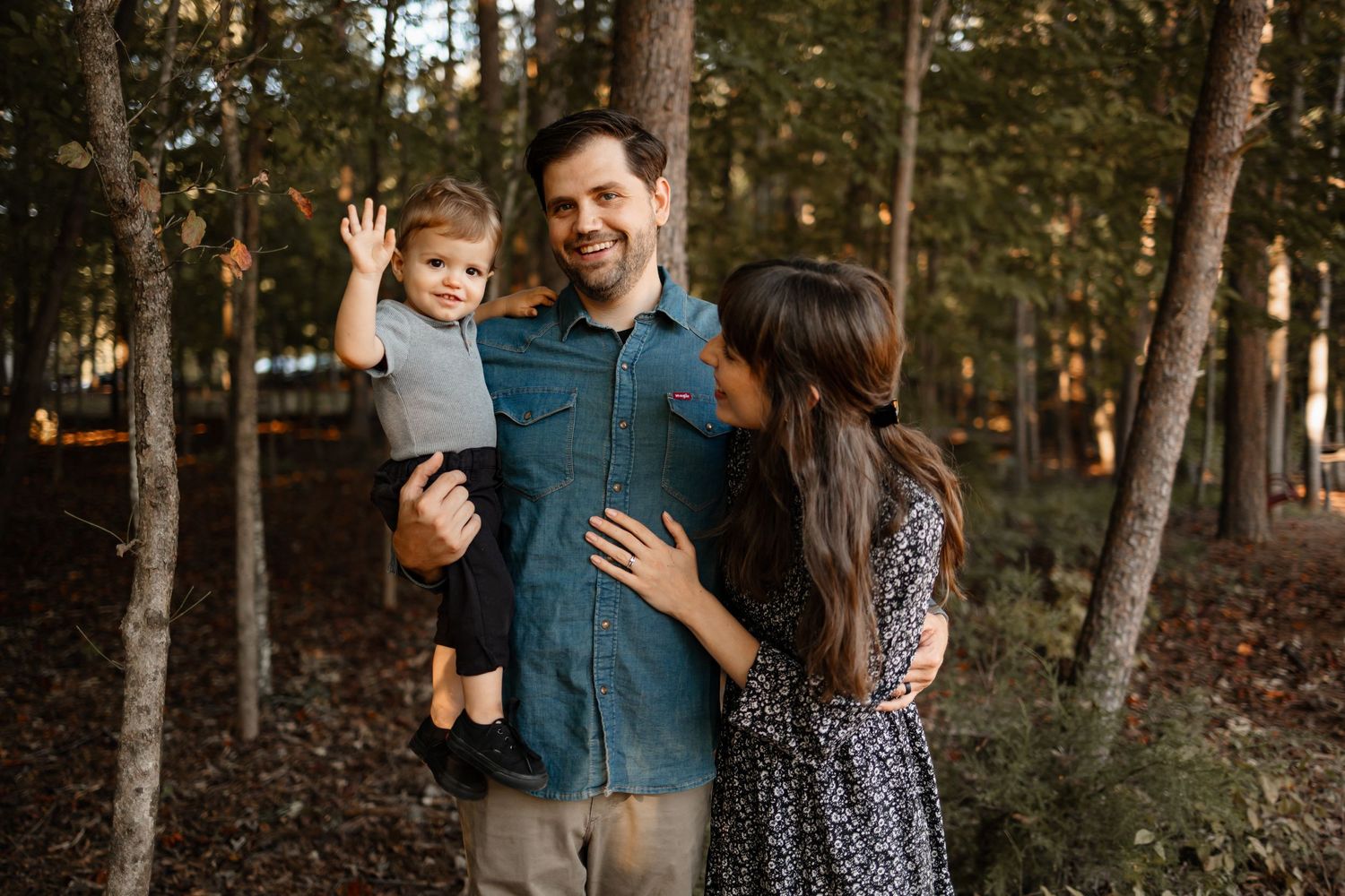A family shares a tender moment together while standing in a scenic wooded forest during golden hour.