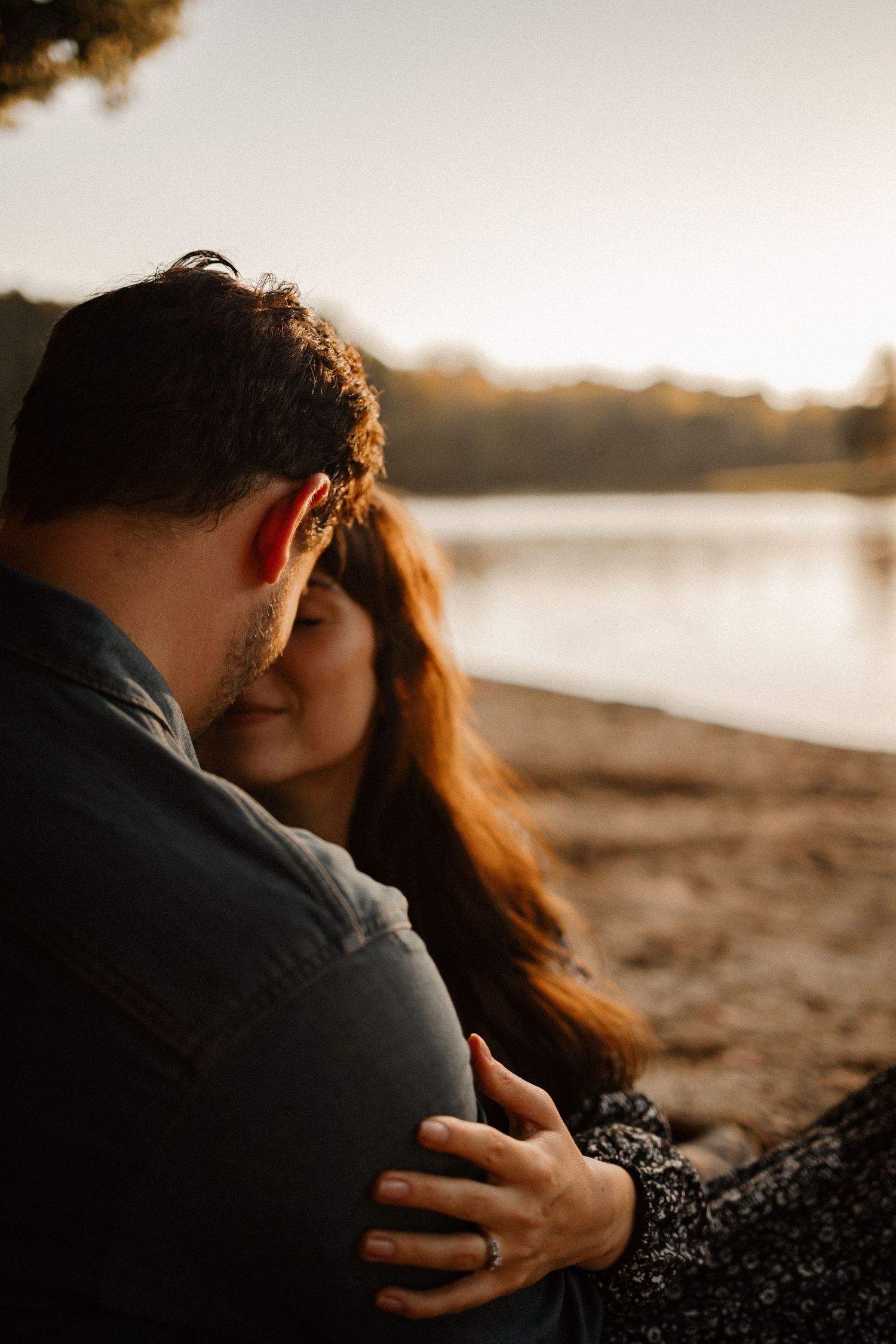 A couple sitting by a lake at sunset intimately close