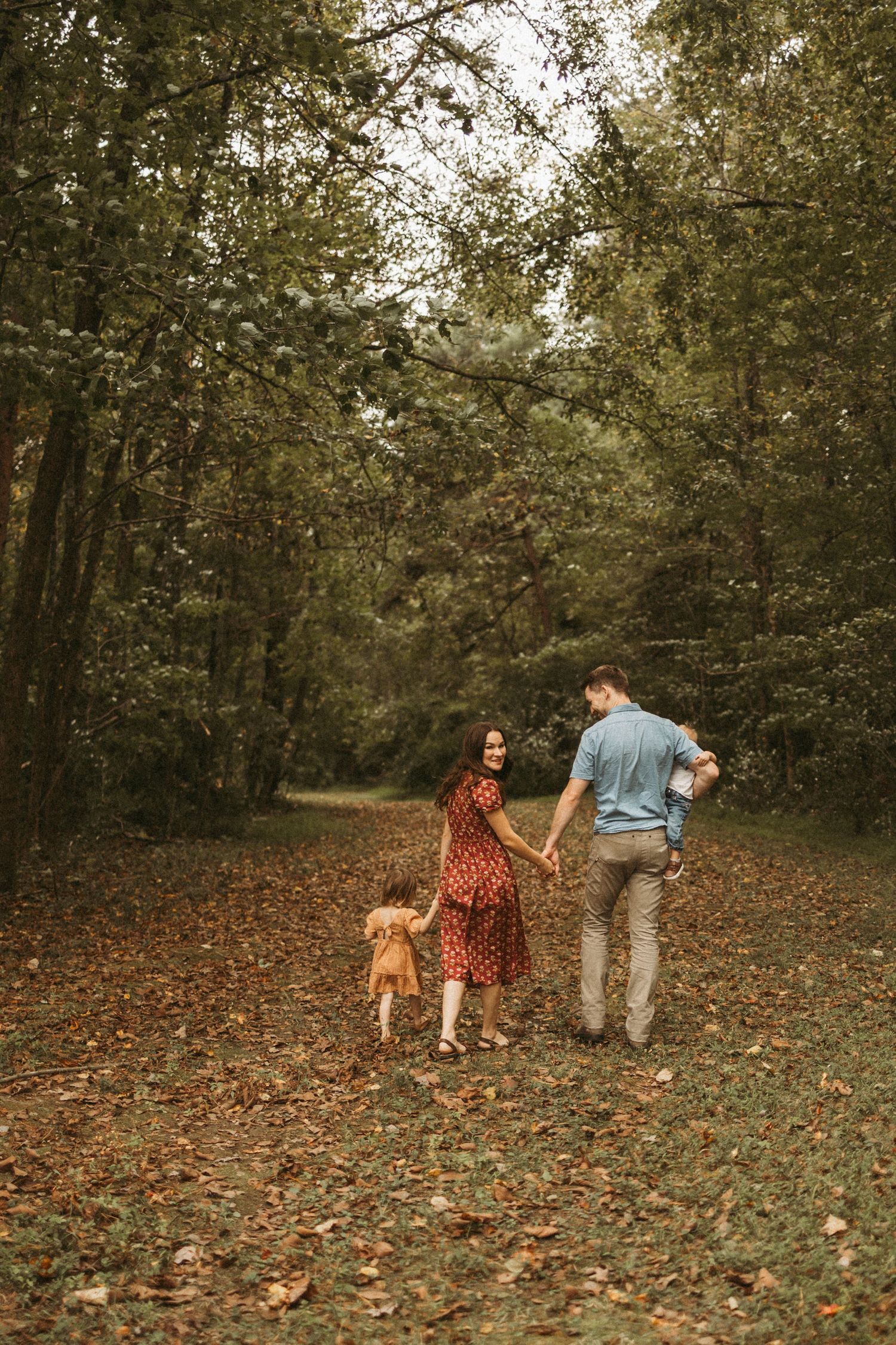 Family walking with their dog on a leaf-covered forest path during autumn.