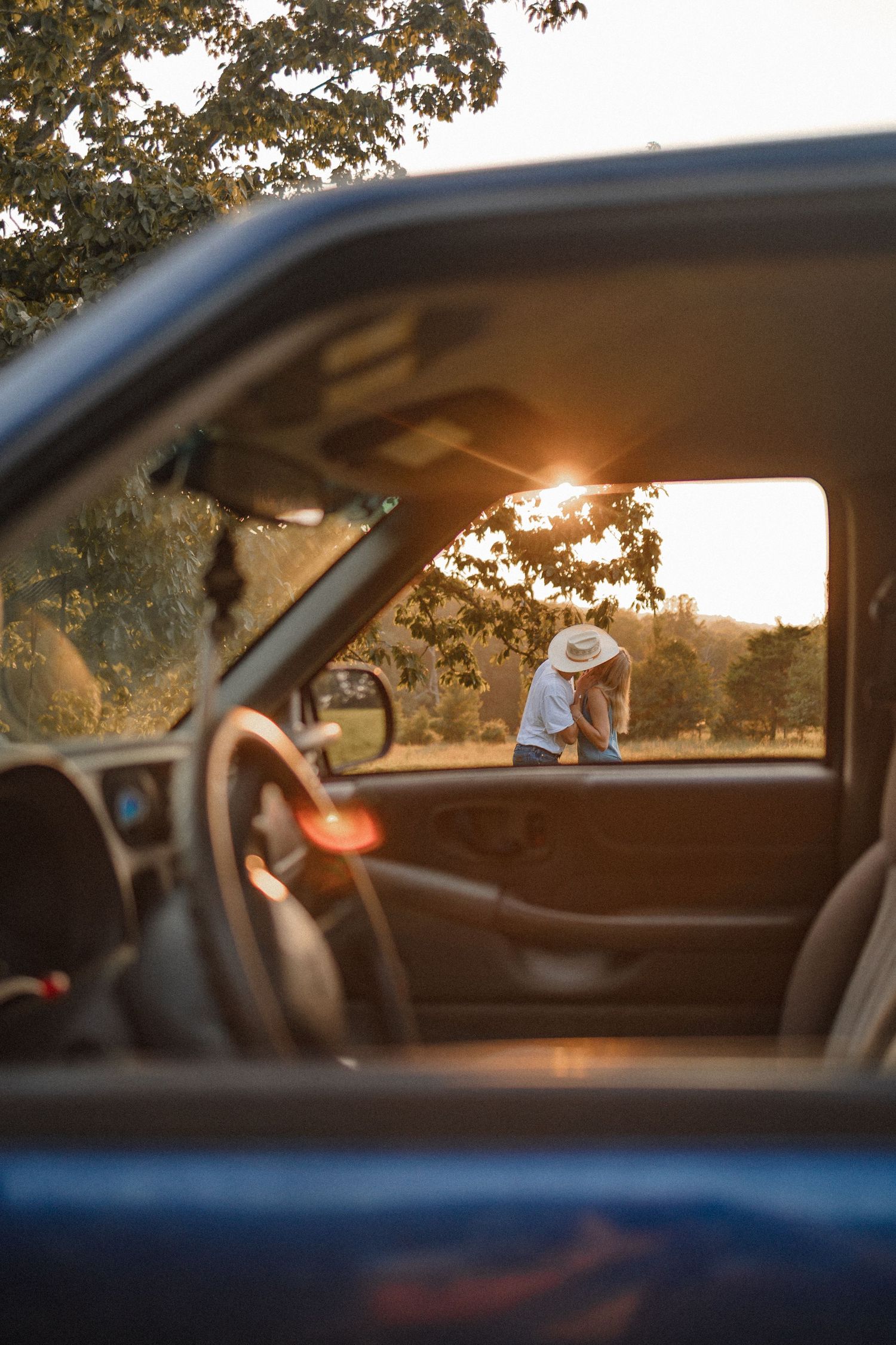 Silhouetted car interior view through window at sunset with warm golden light filtering through trees.