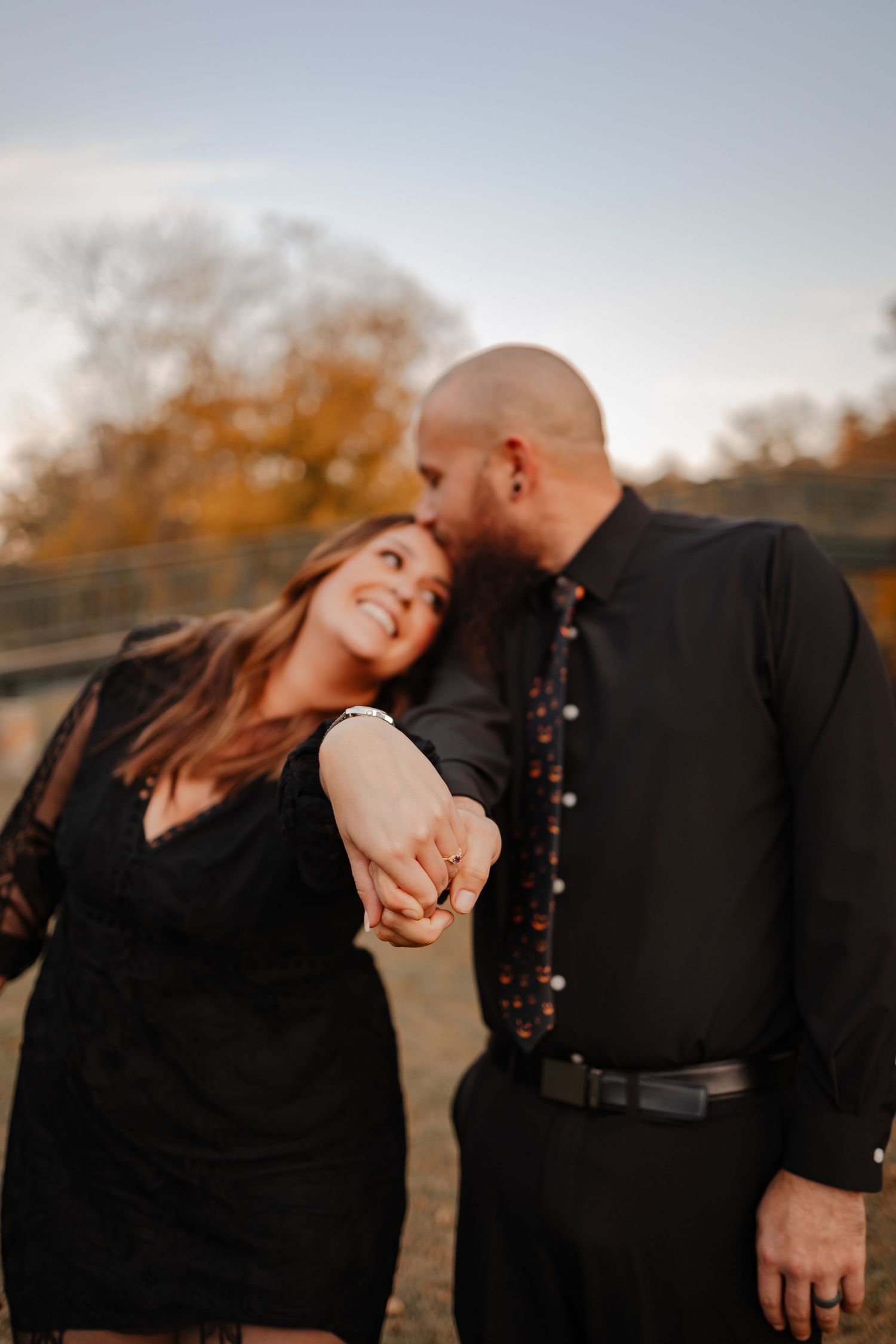 A man kissing the head of his fiance as she holds out her engagement ring