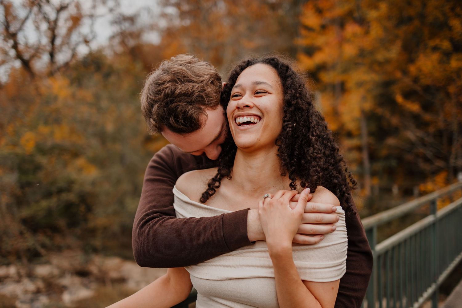 A couple hugging and laughing with fall trees behind them