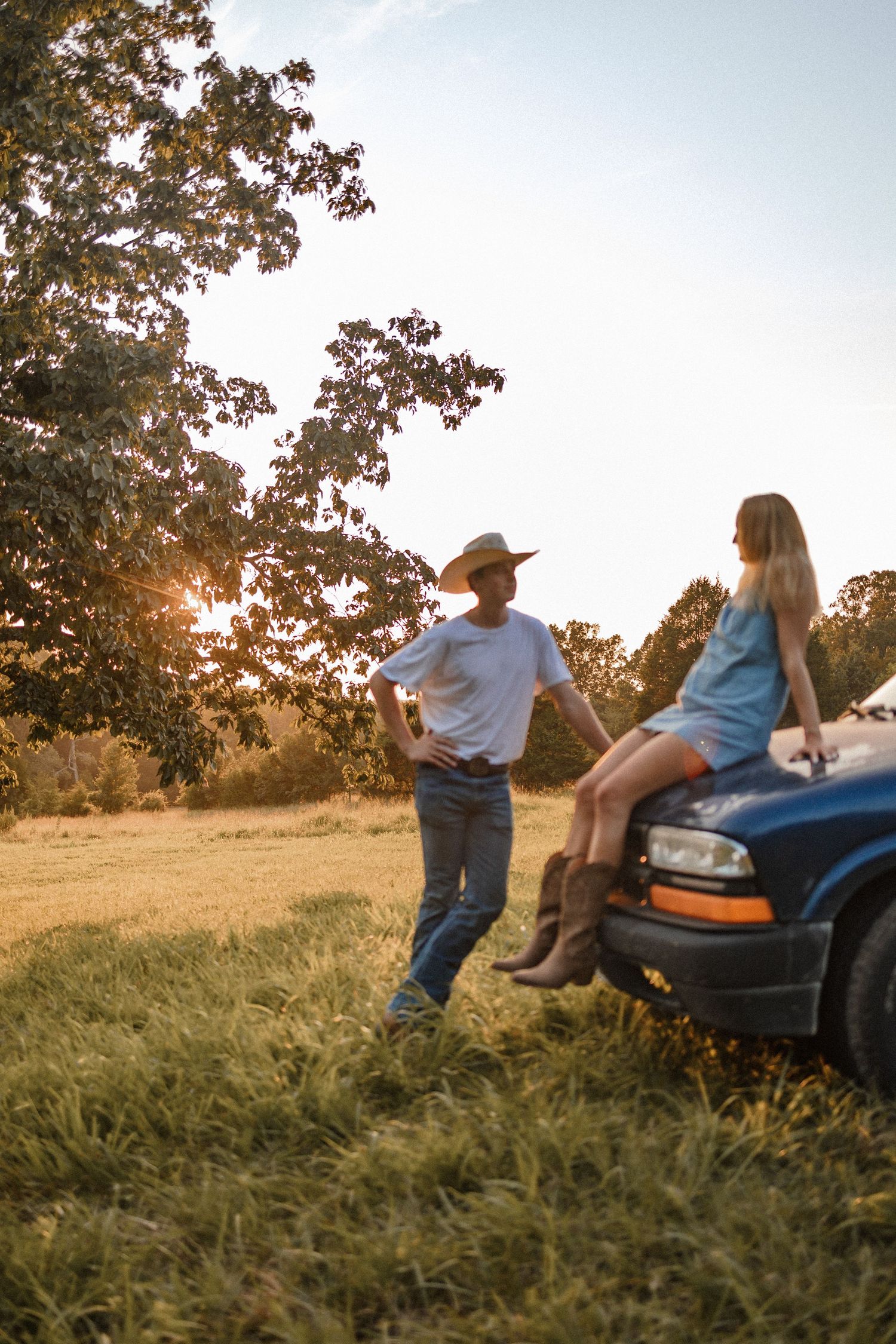 People sitting on a riding lawn mower in a grassy field at sunset with golden light filtering through trees.