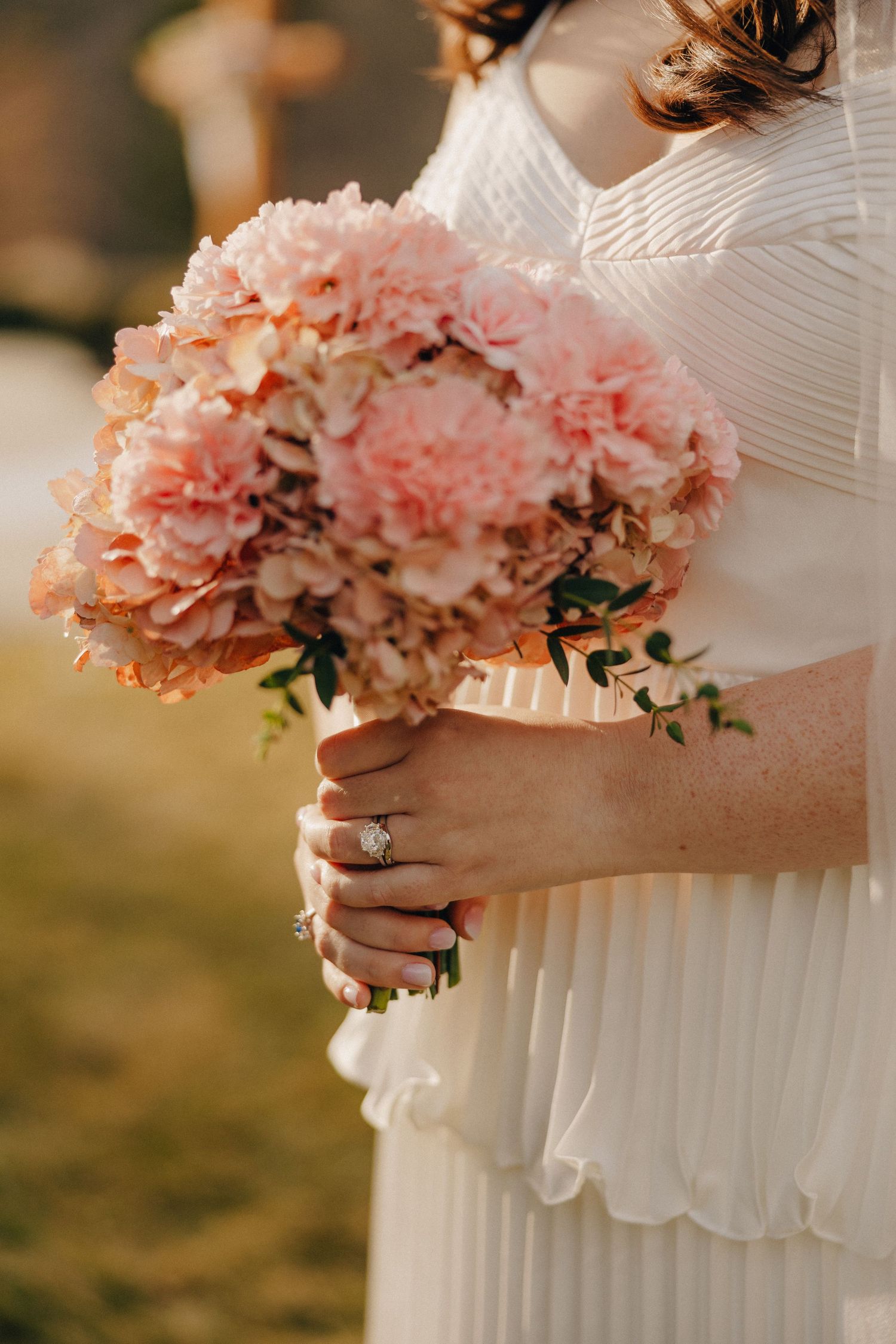 Close-up of pink floral bouquet held against pleated white dress.