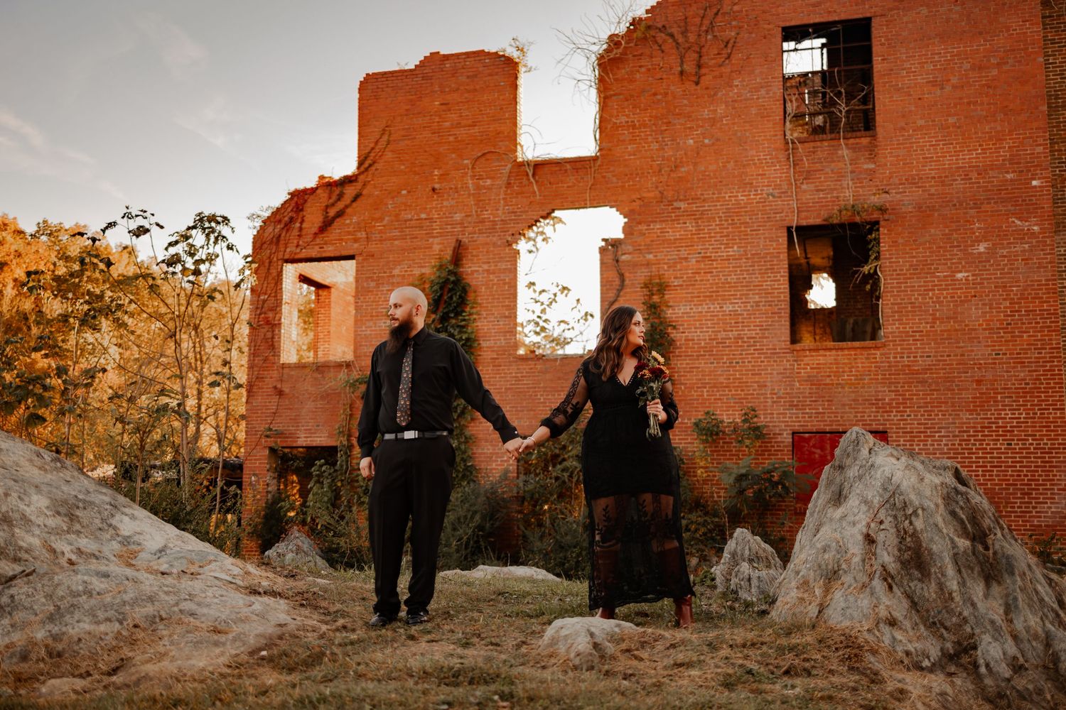 A couple holding hands in front of a old brick building looking in different directions