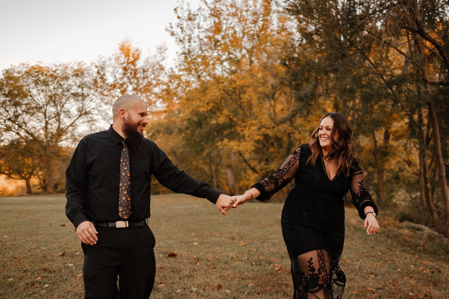 A couple walking and holding hands laughing and looking at each other with fall foliage behind them