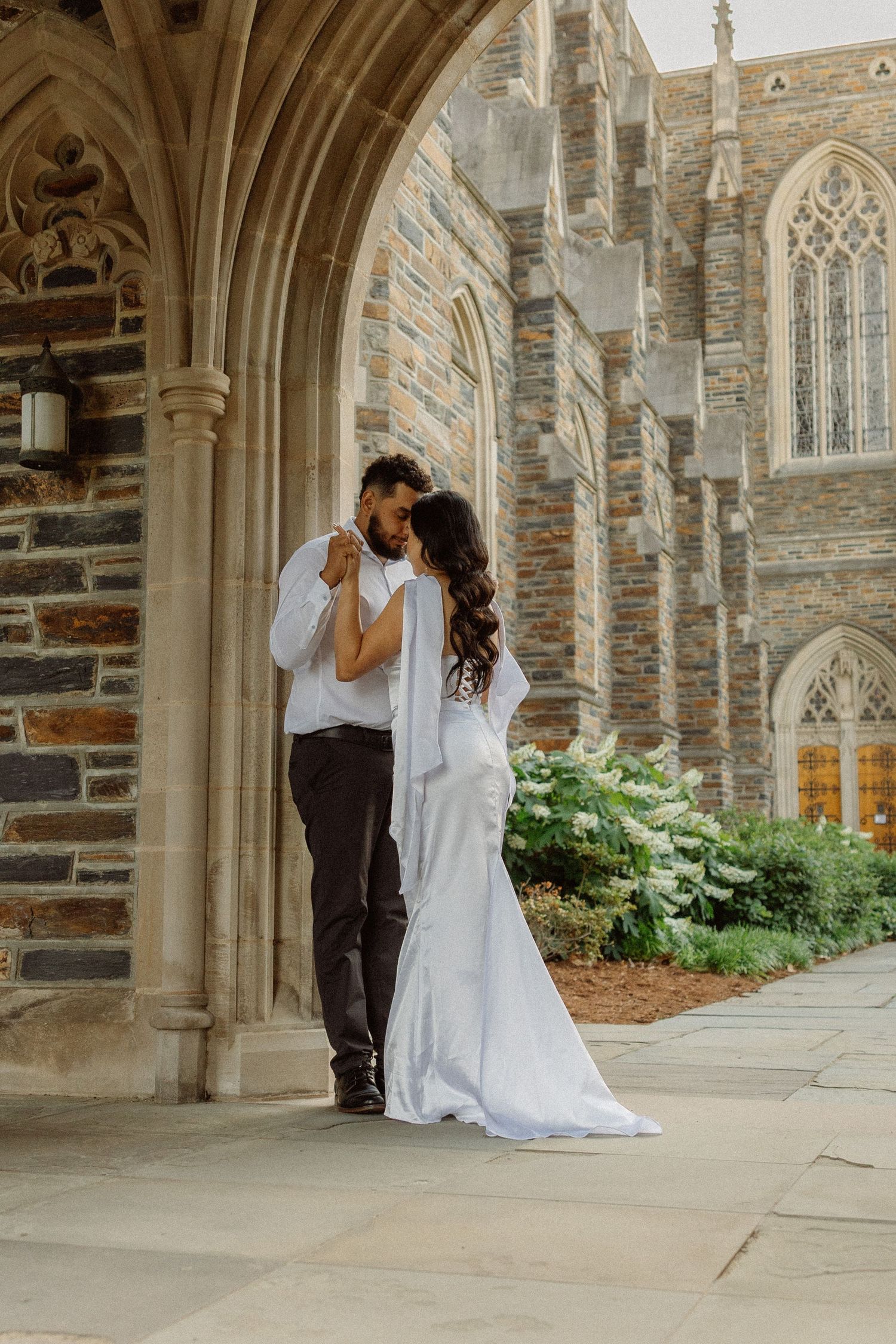 A bride and groom share a romantic embrace under a stone archway at Duke Chapel in Durham, North Carolina.