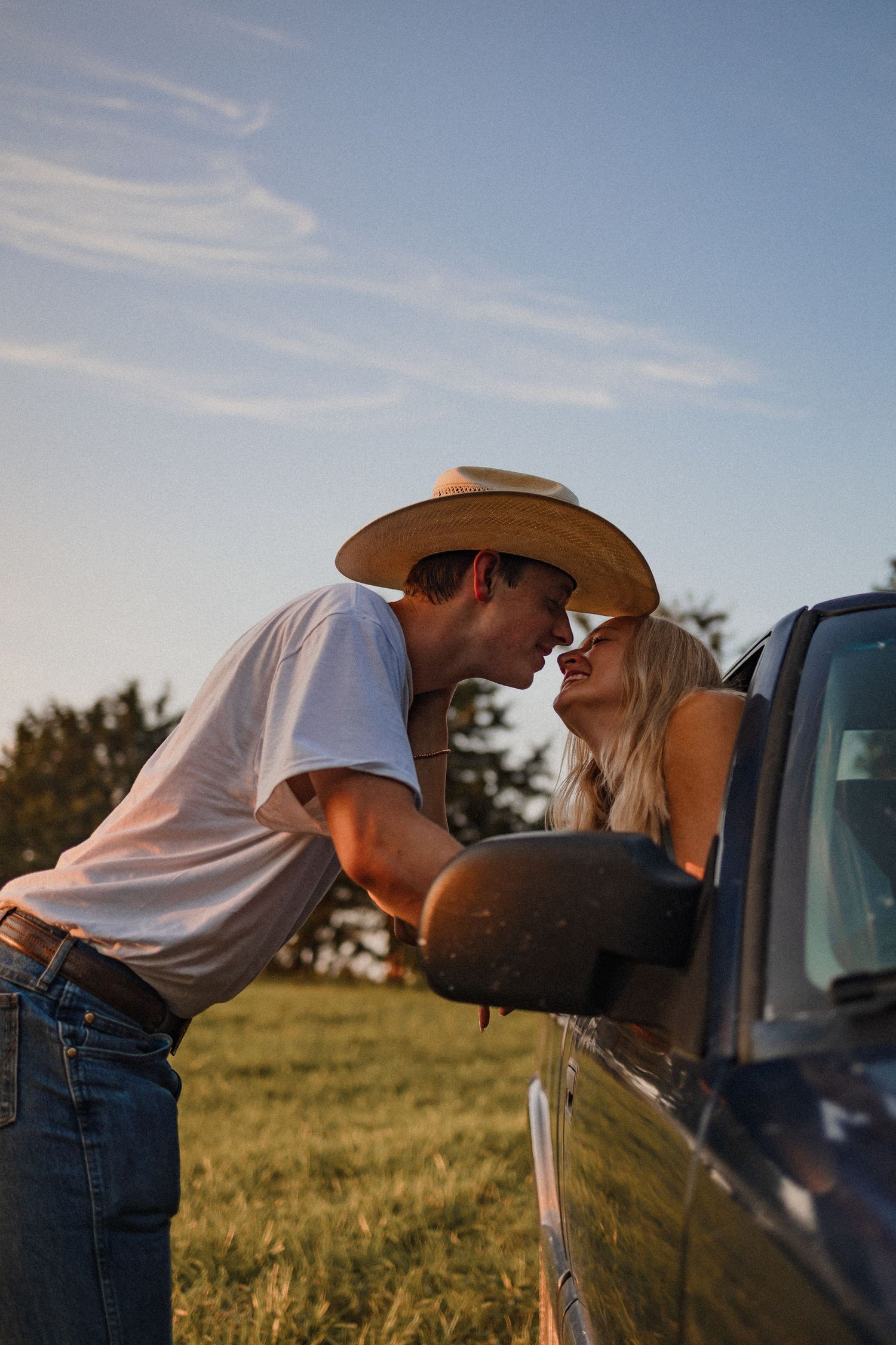 A sequence showing a person in a cowboy hat leaning into a truck window in a grassy field during sunset.