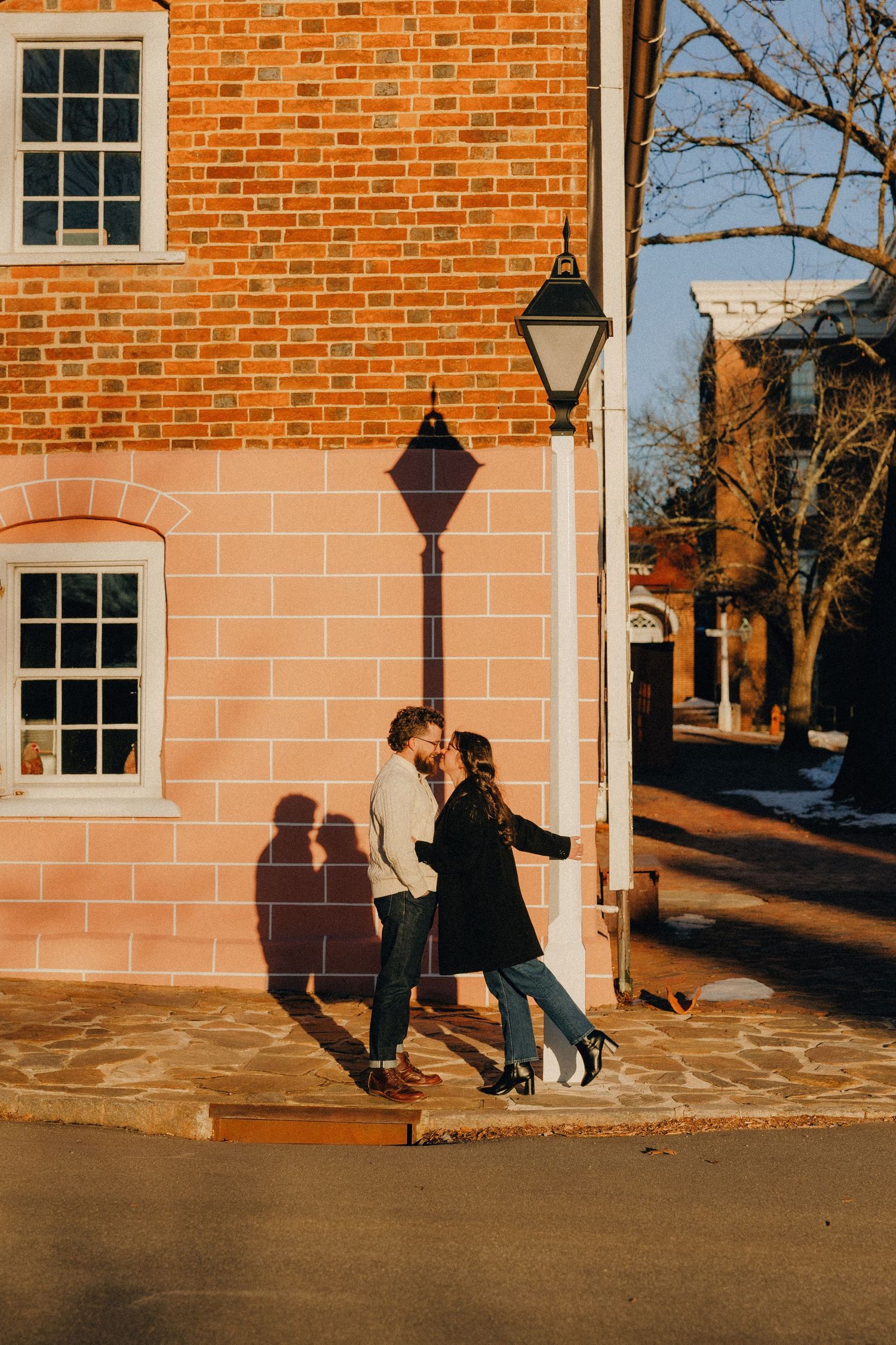 Romantic moment captured against brick building exterior in warm evening light.