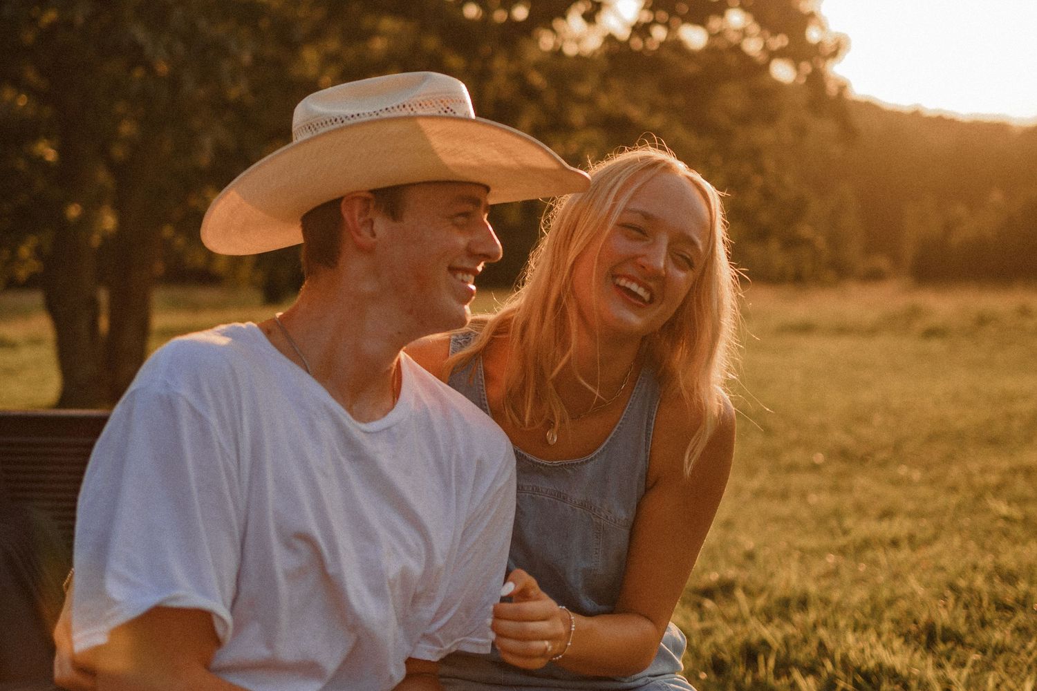 Couple sharing tender moments in a golden sunset field while wearing casual summer attire.