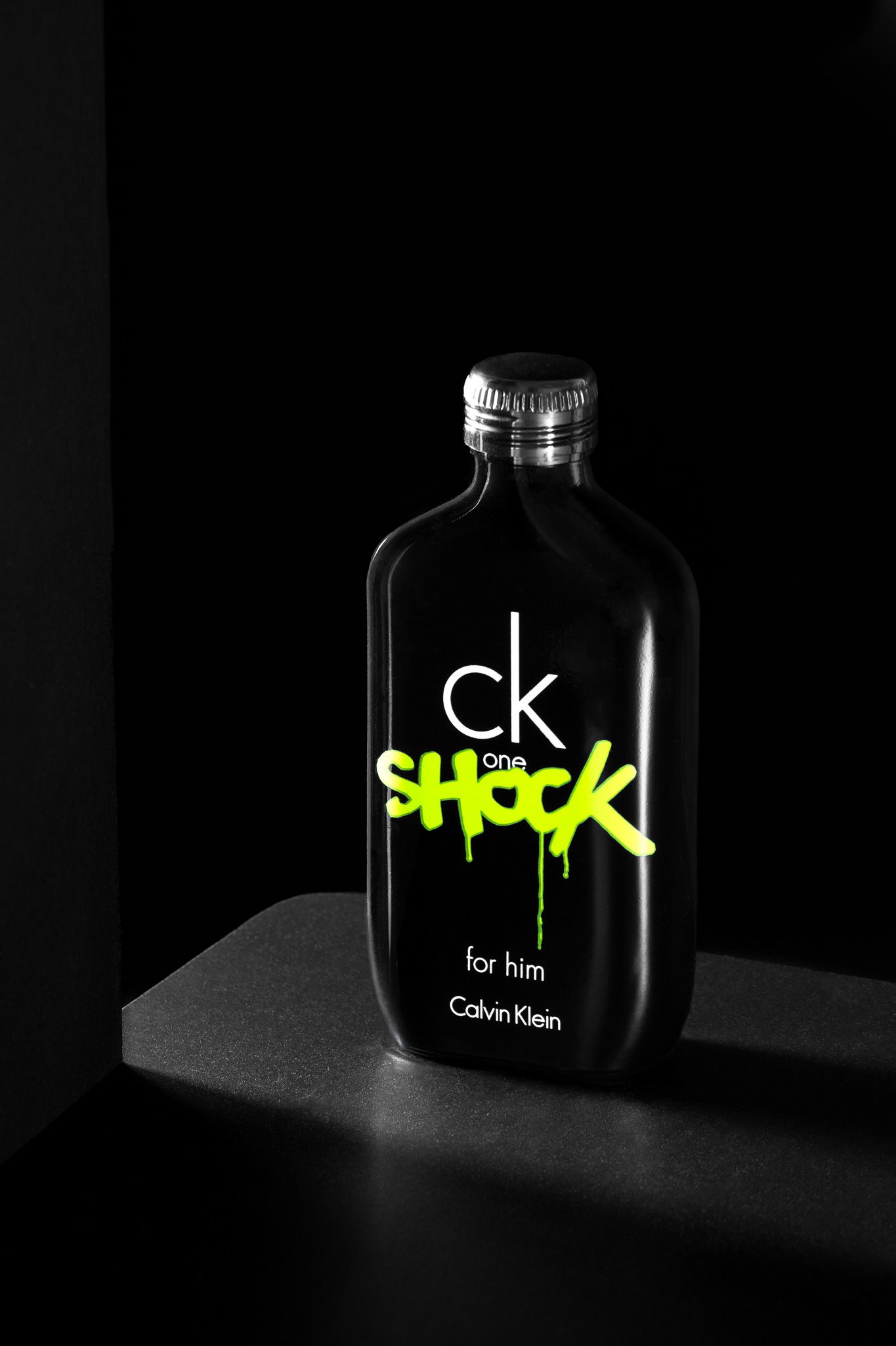 CK One Shock for Him Calvin Klein cologne bottle in black with neon green logo on dark background.