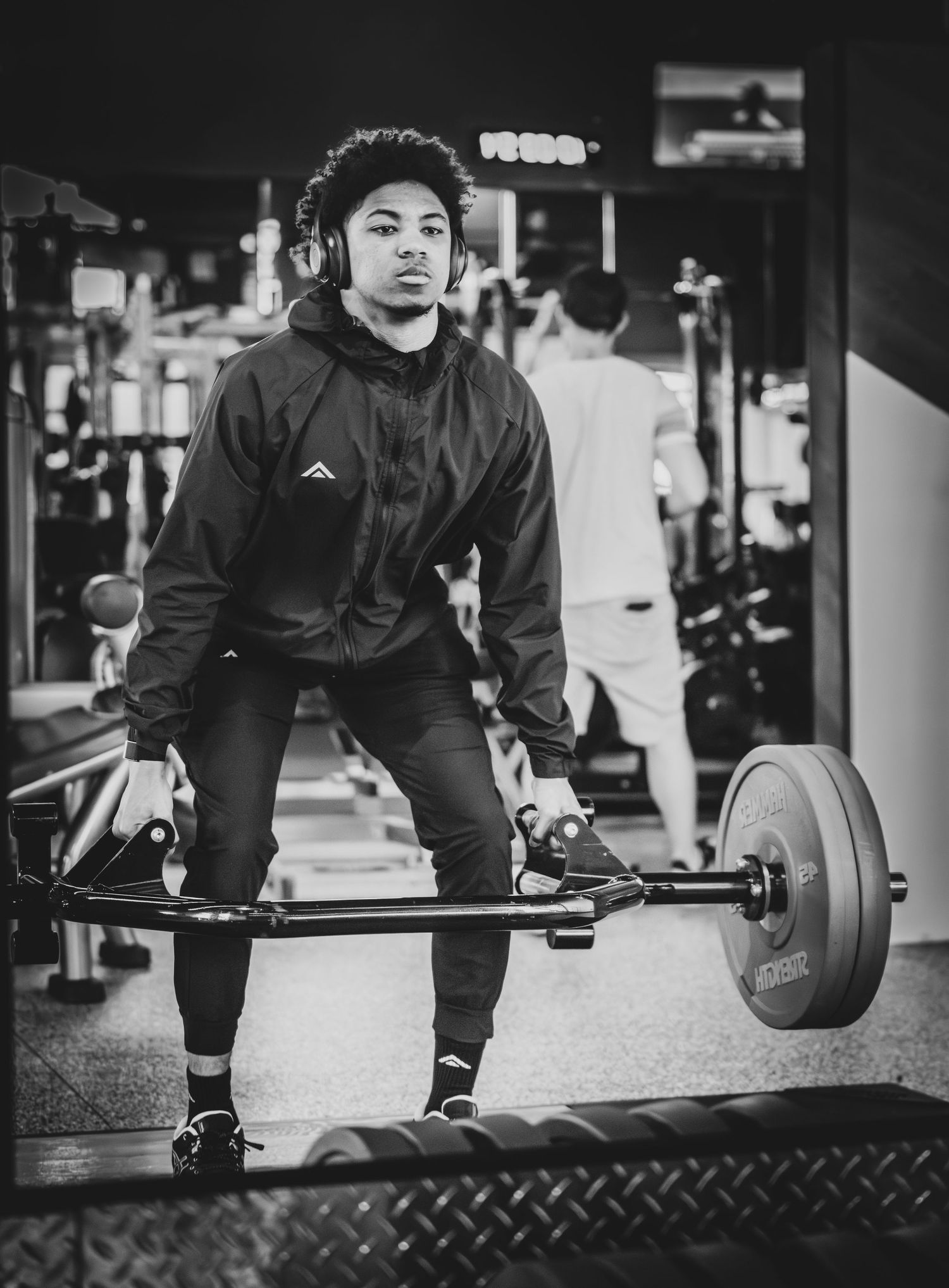 Black and white photo of a young athlete performing a deadlift with a barbell in a gym.