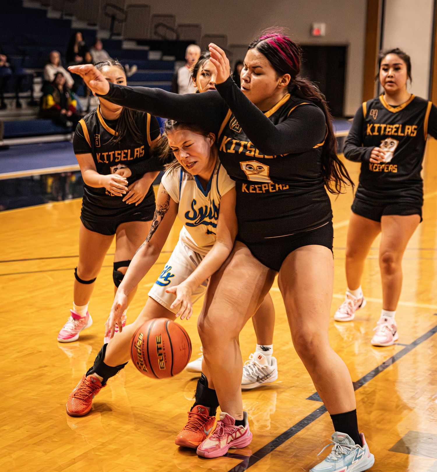 Female basketball players in a competitive game, with Kitselas team defending against a player dribbling the ball.