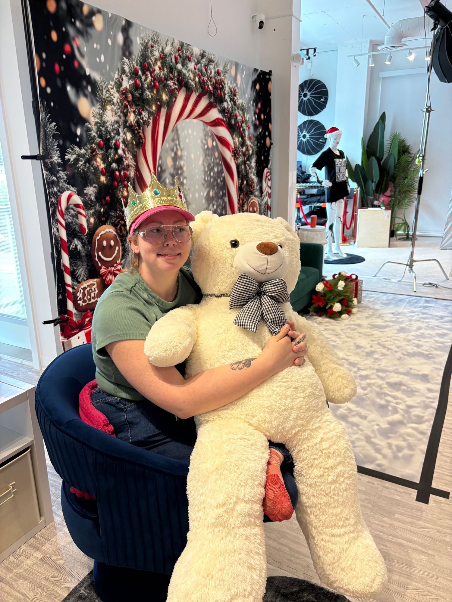 Woman in elf hat hugging large white teddy bear with bow tie in festive Christmas-themed photo studio.